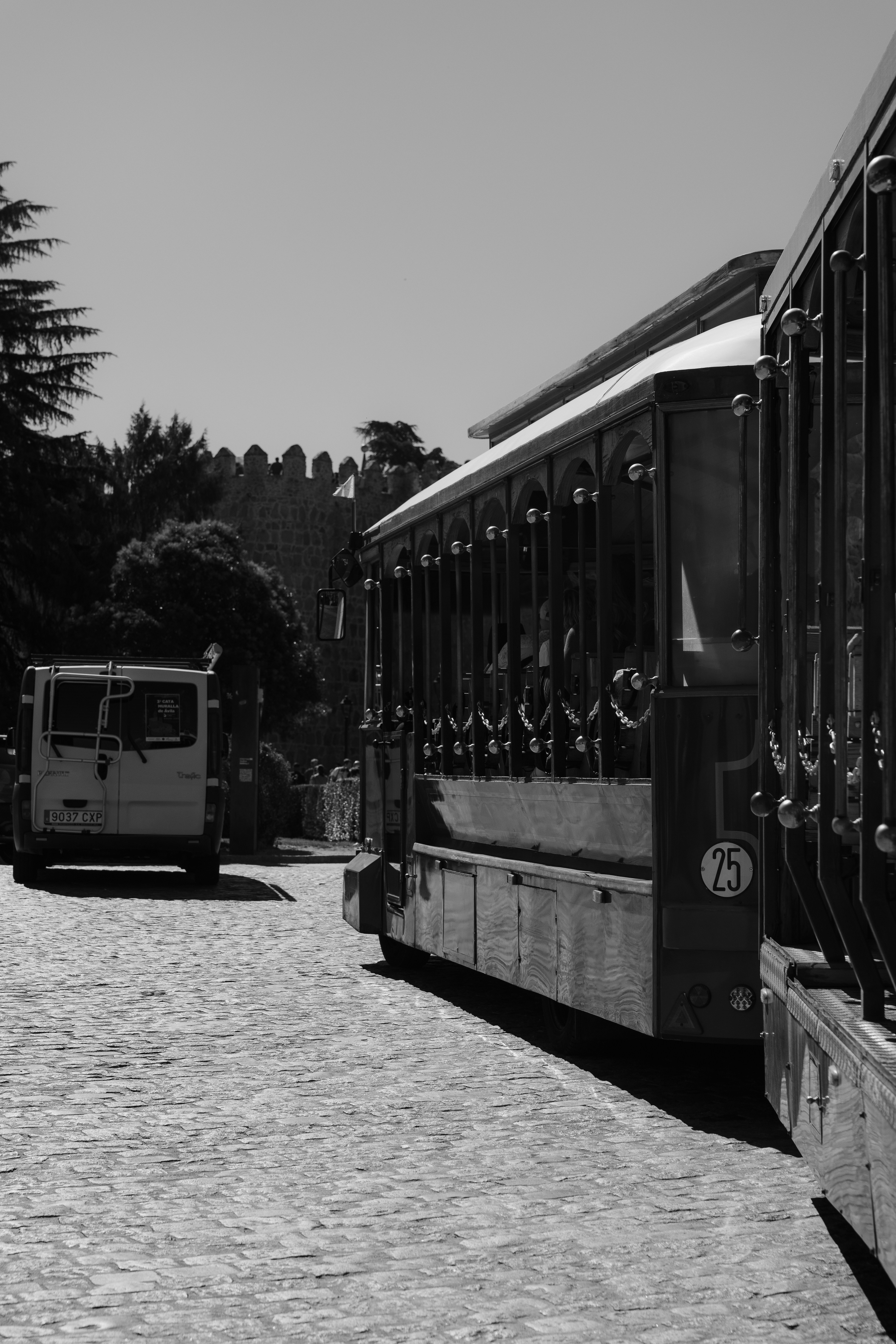 A tourist tram on a cobblestone street near a stone wall in Avila
