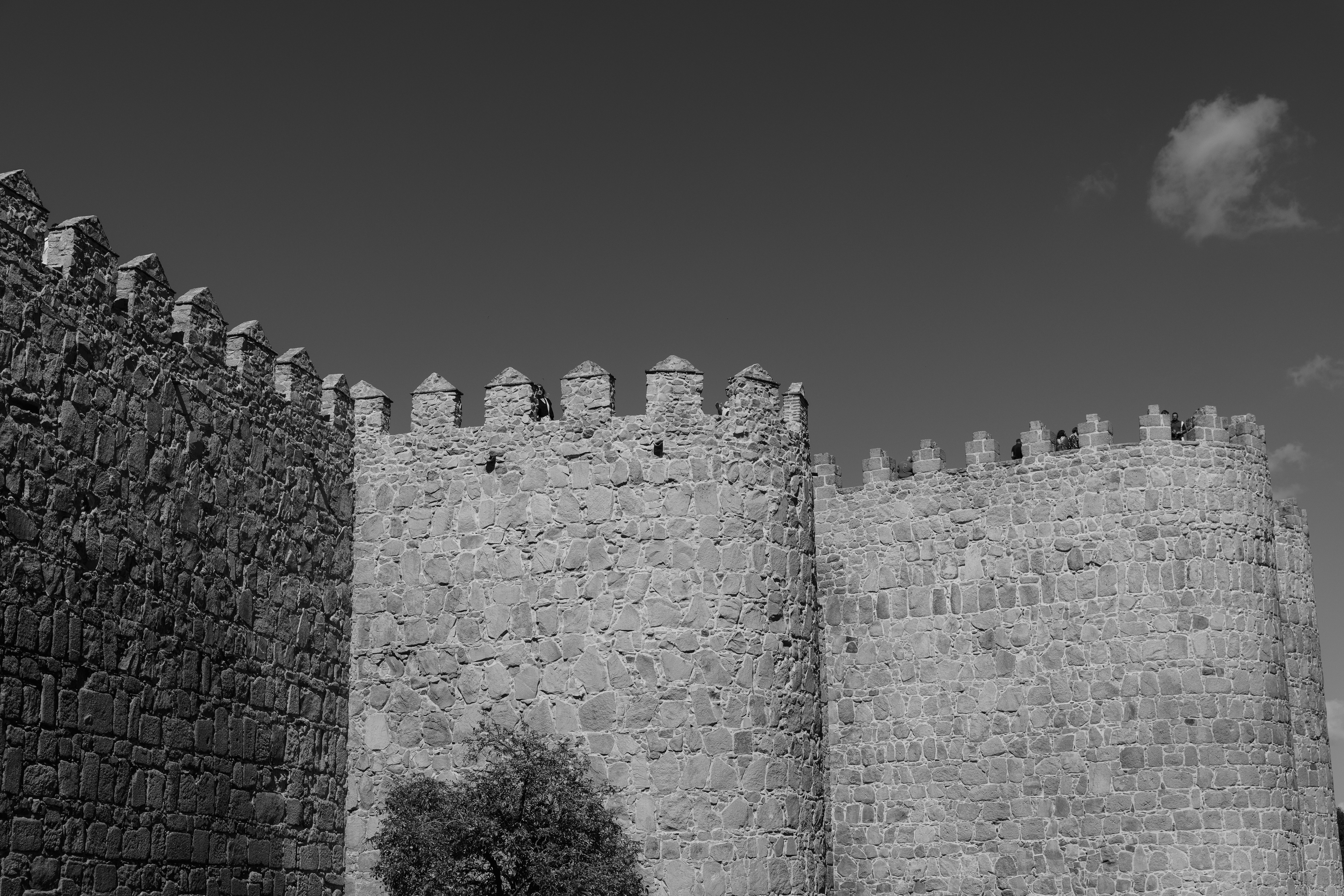 A black and white view of stone medieval castle walls with crenelated battlements