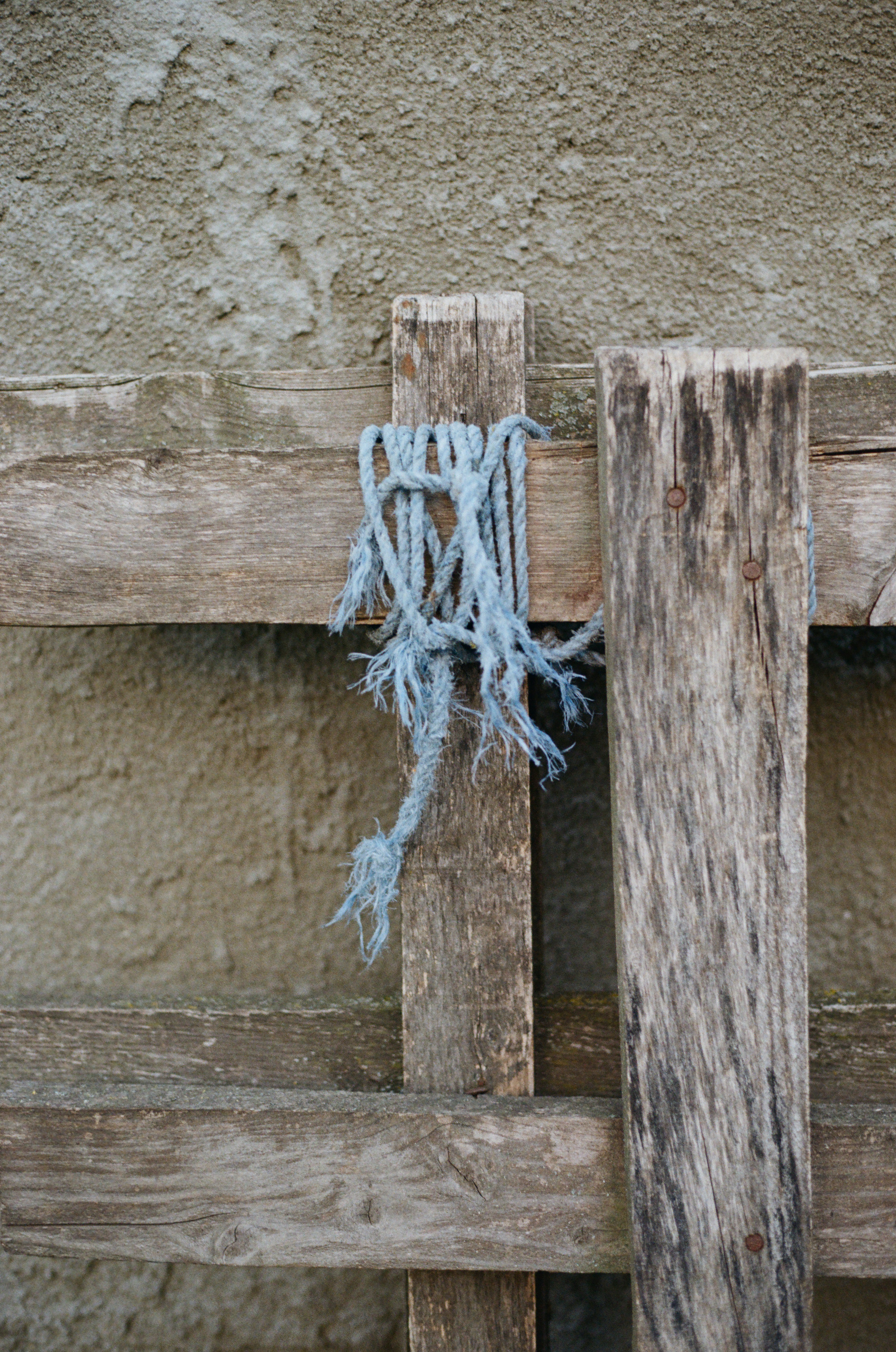 A frayed blue rope tied around a weathered wooden fence post