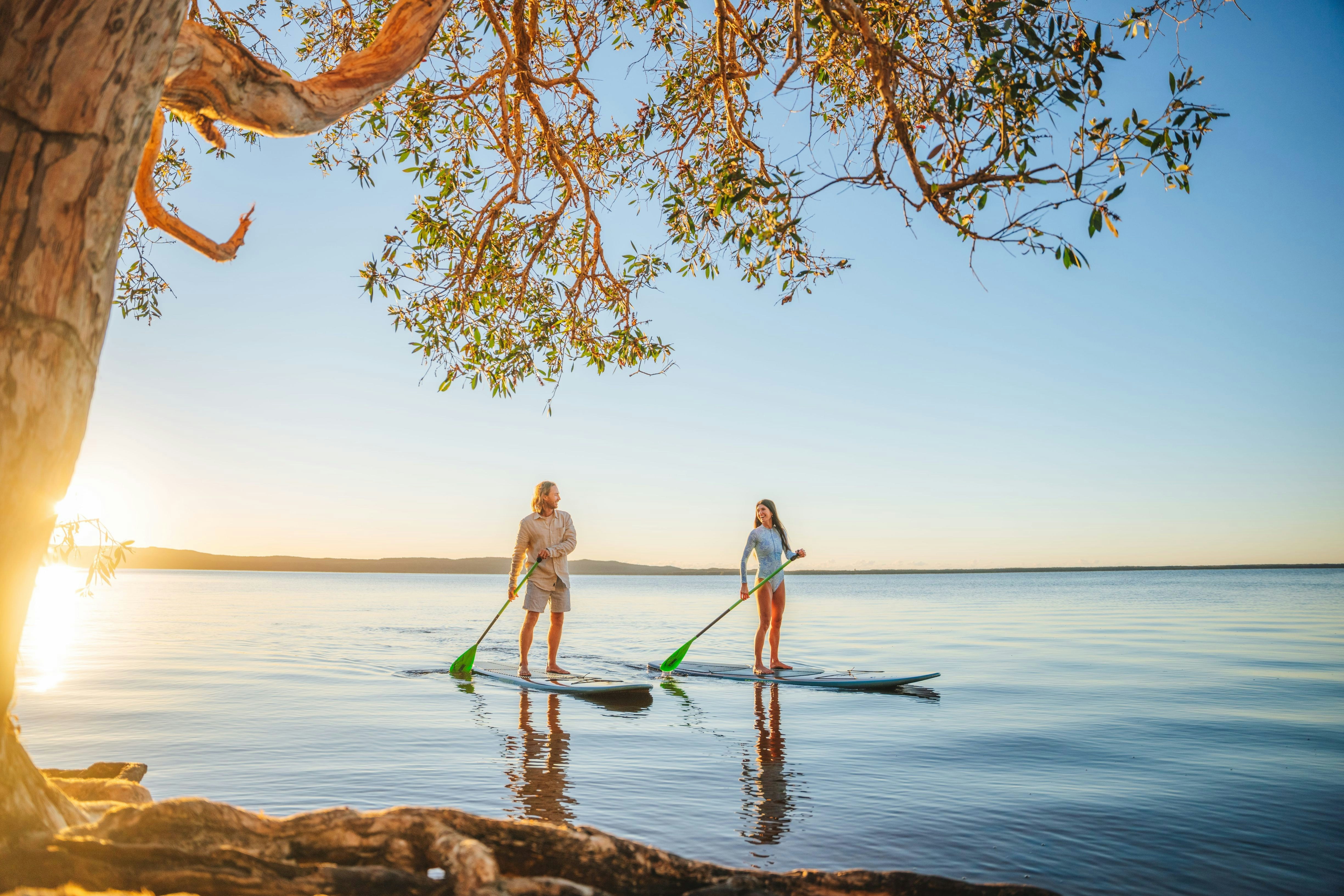 A man and a woman paddleboarding on a calm lake during golden hour