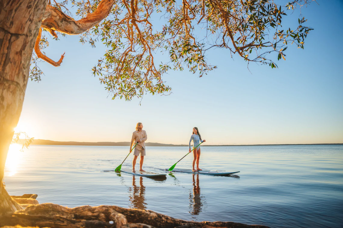 Two people enjoying stand-up paddleboarding on a peaceful lake at golden hour