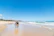A man and a woman walking along a sandy beach under a clear sky