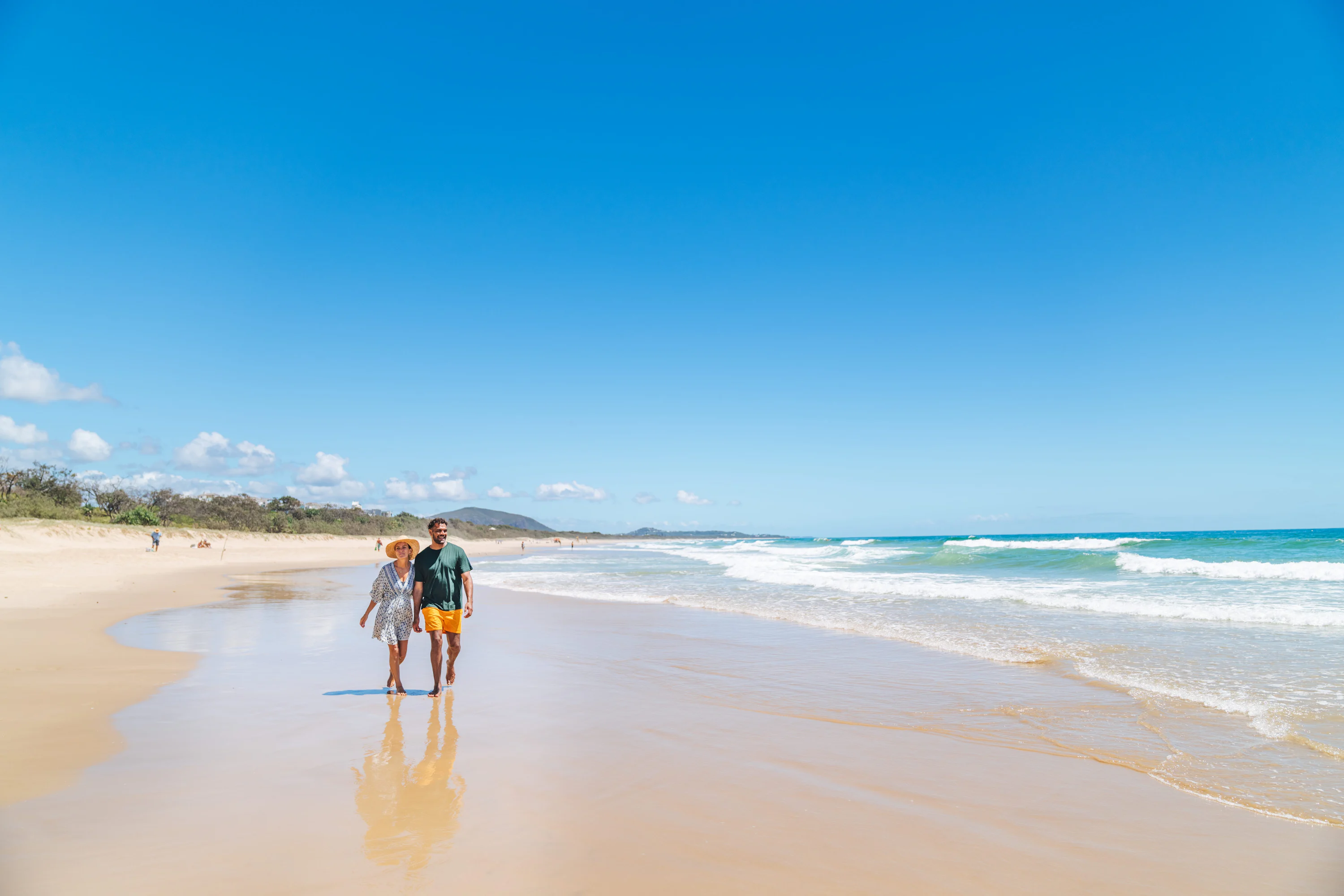 A man and a woman walking along a sandy beach under a clear sky