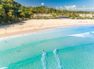 Aerial view of people swimming and paddleboarding in clear turquoise water at Noosa Main Beach
