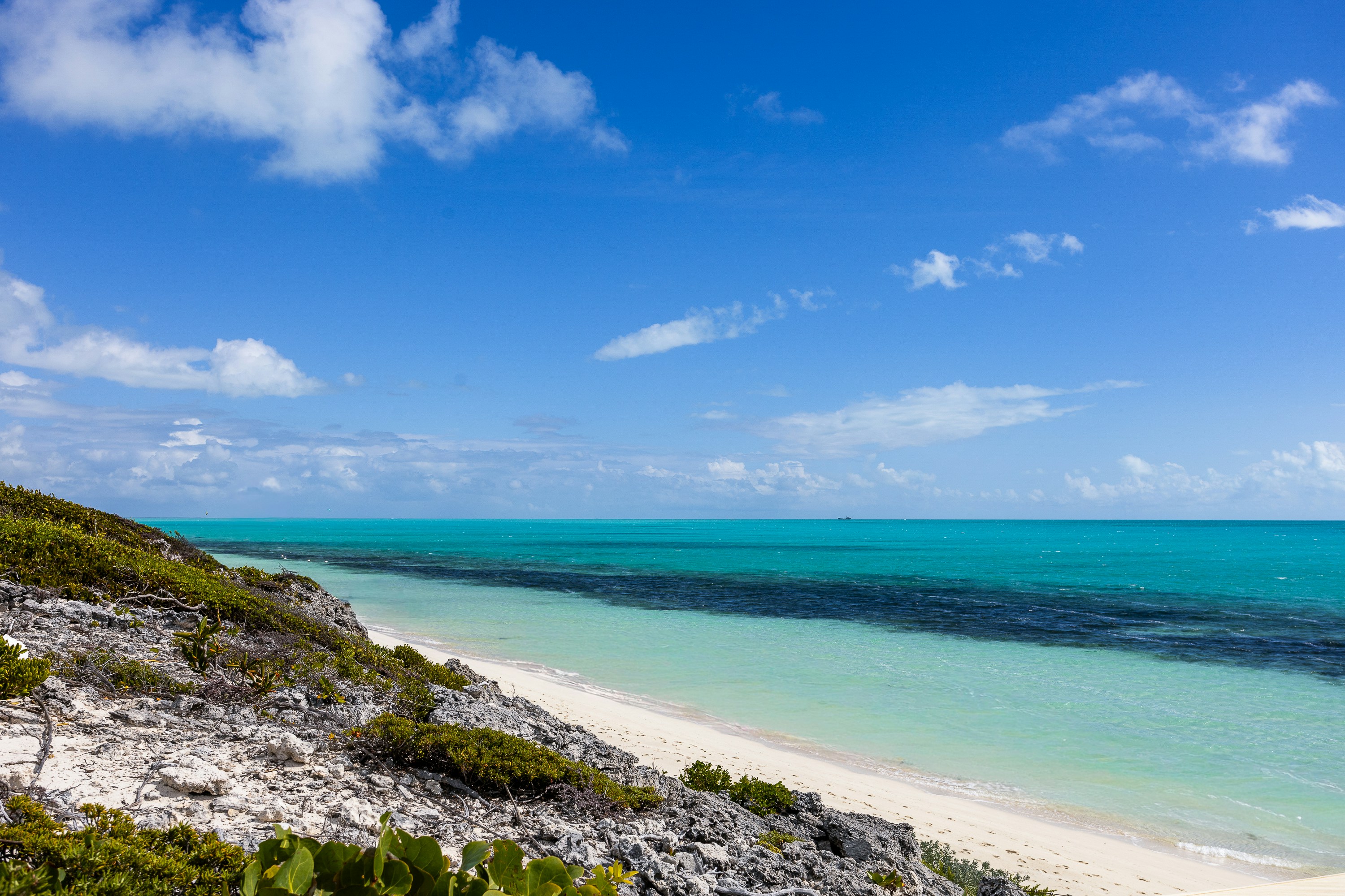 A rocky coastline with green vegetation overlooking a turquoise sea under a blue sky