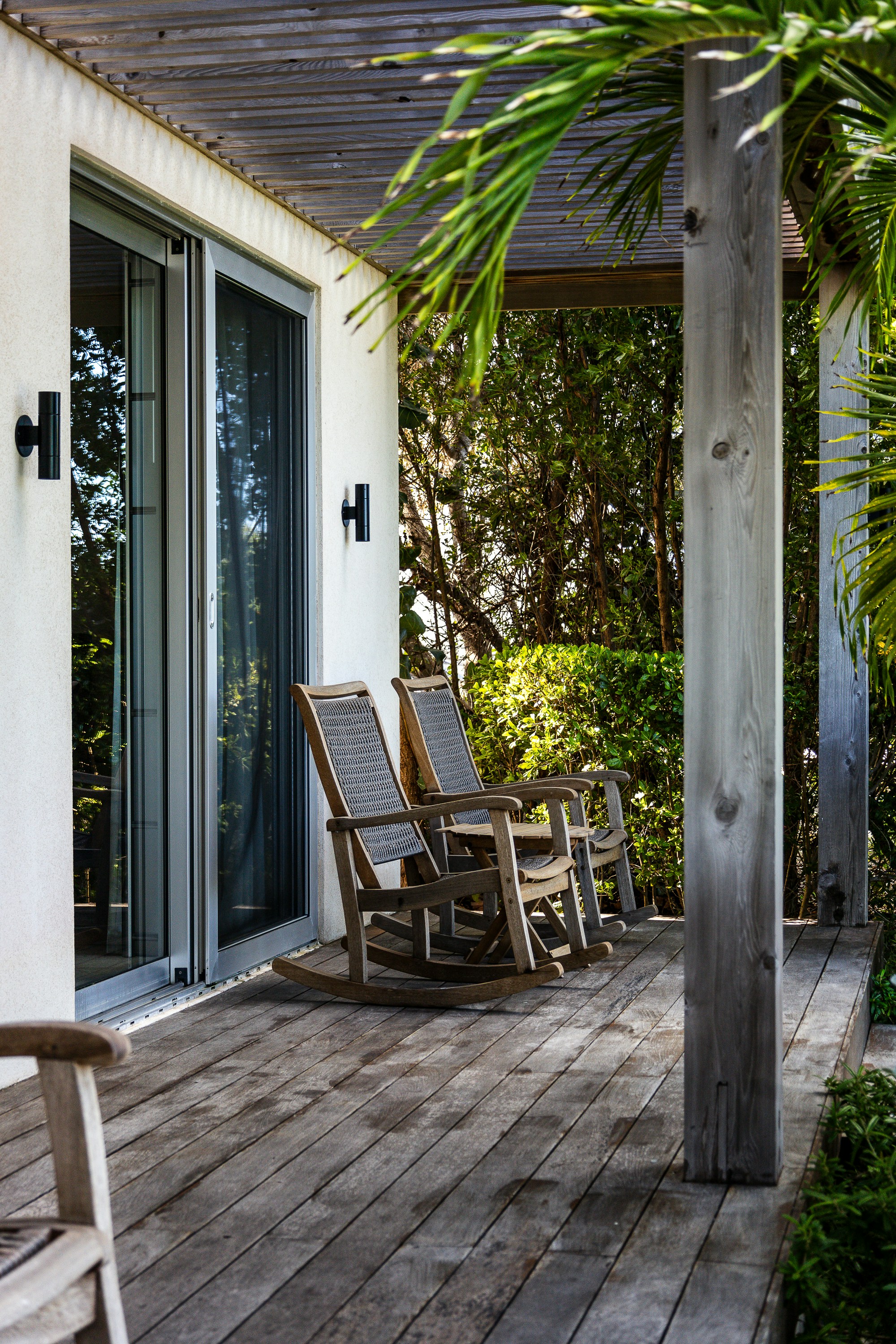 Two wooden rocking chairs on a weathered deck outside a glass sliding door