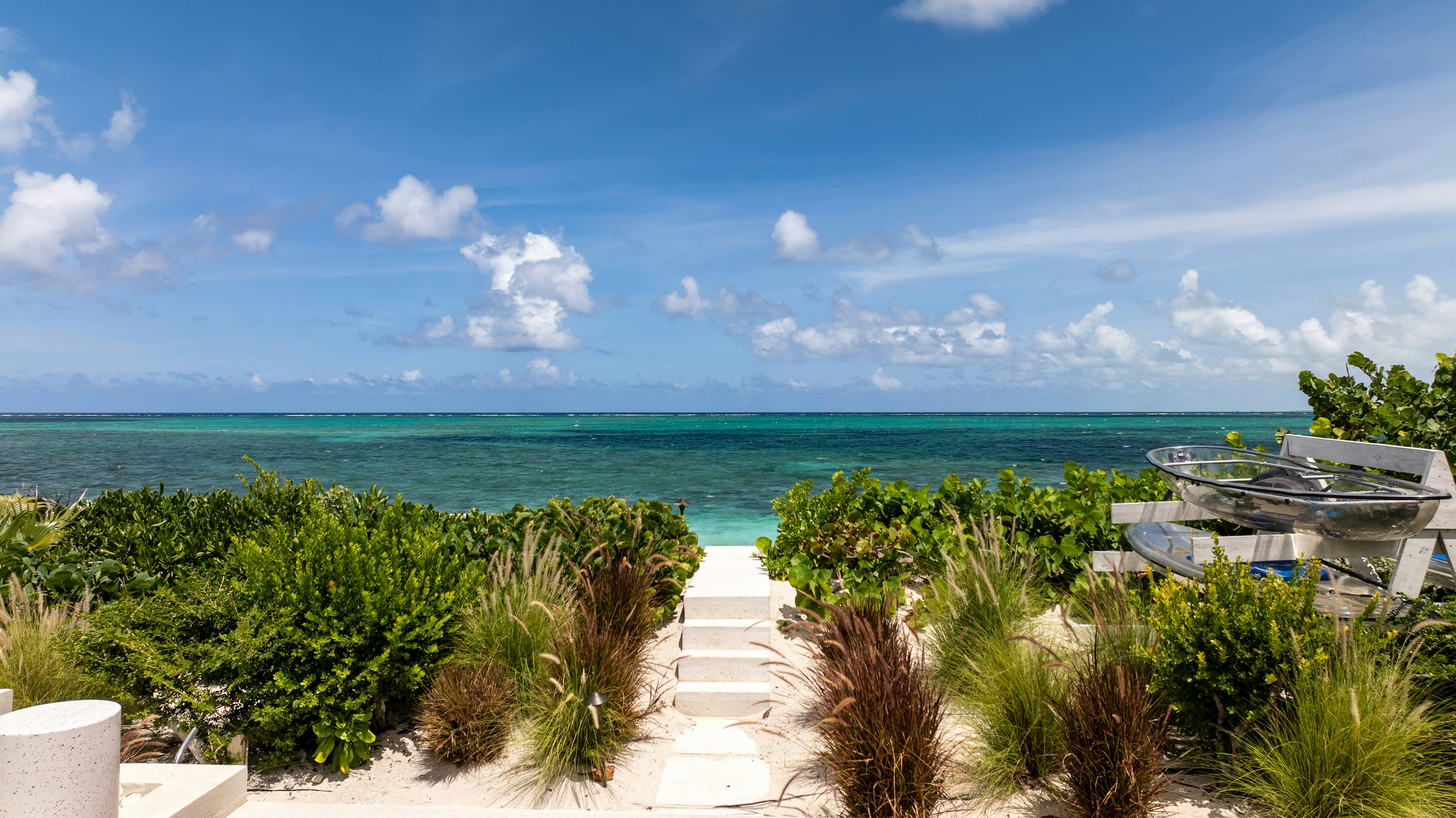 Concrete steps leading through coastal vegetation to a turquoise sea under a blue sky