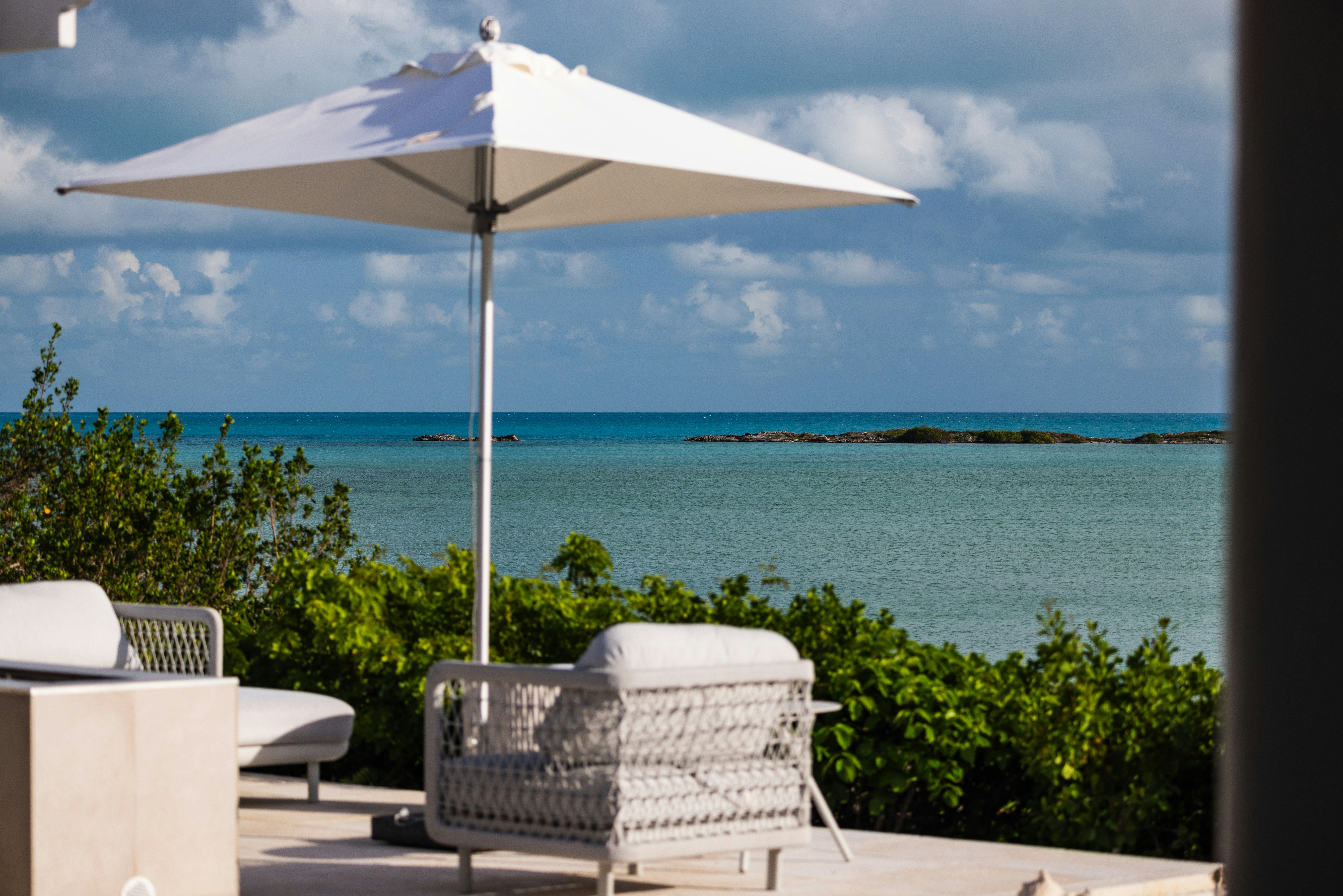 A white umbrella and lounge chairs on a terrace above a calm turquoise sea