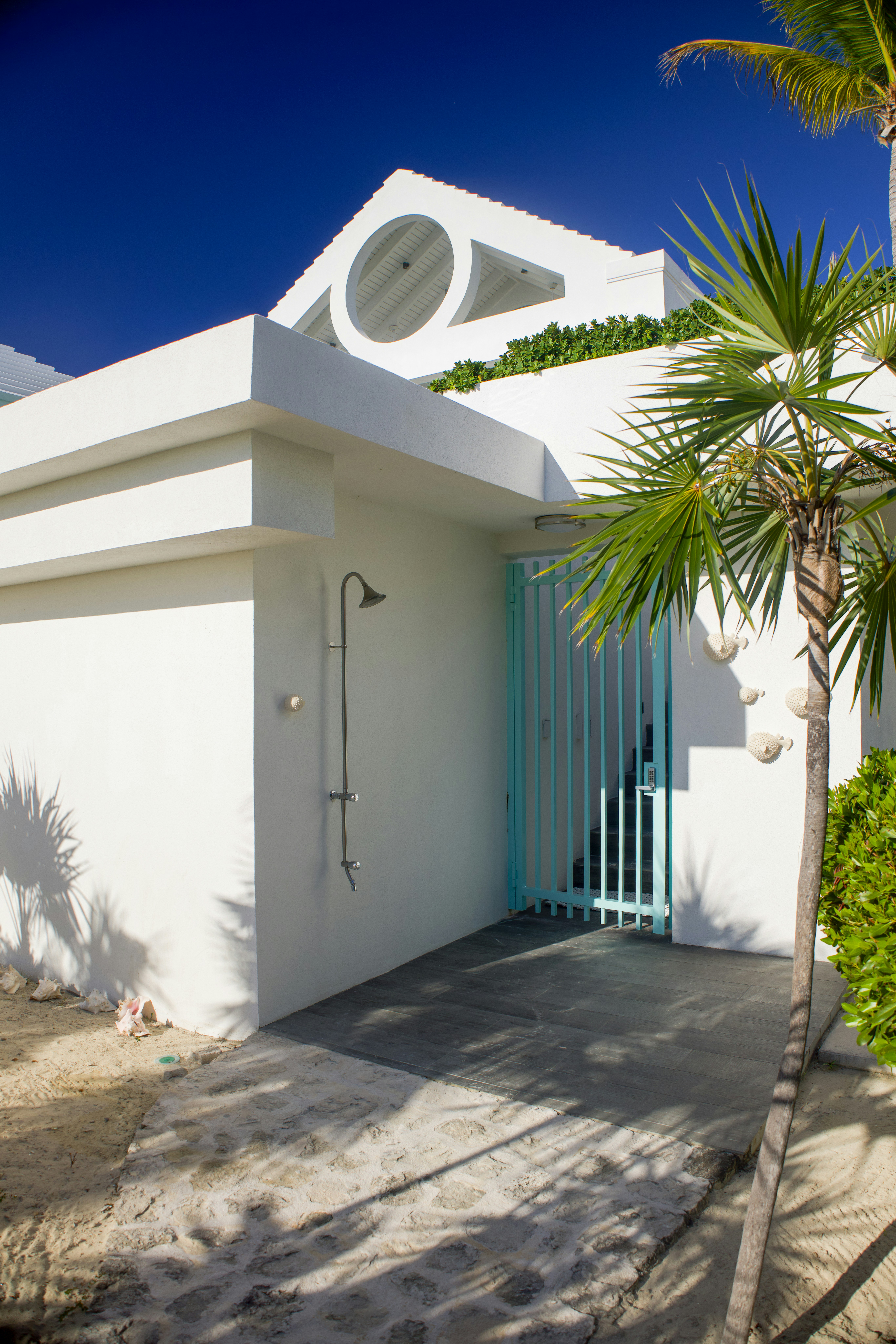 A white building with an outdoor shower and a light blue gate