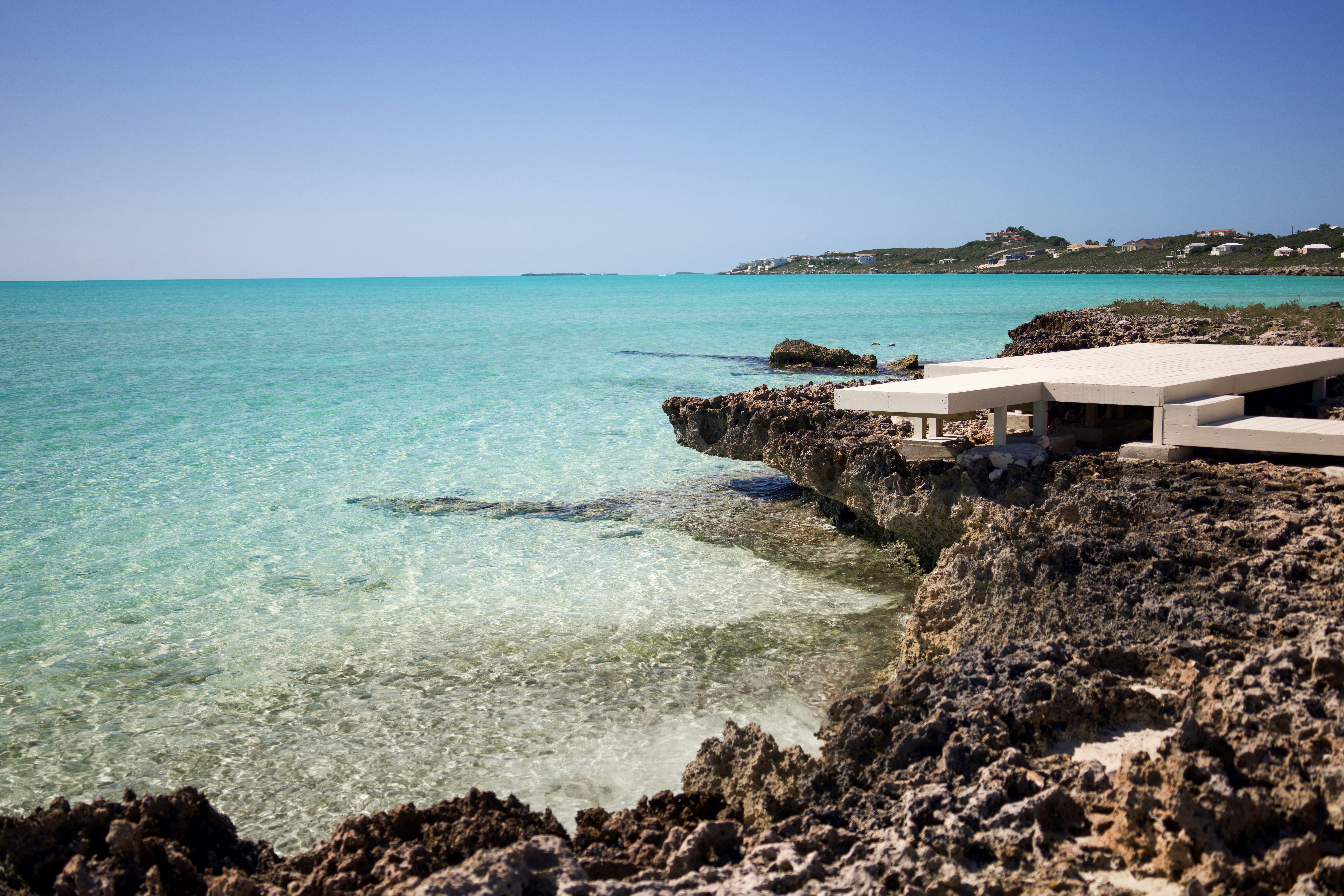 A white wooden deck on a rocky shoreline overlooking clear turquoise water