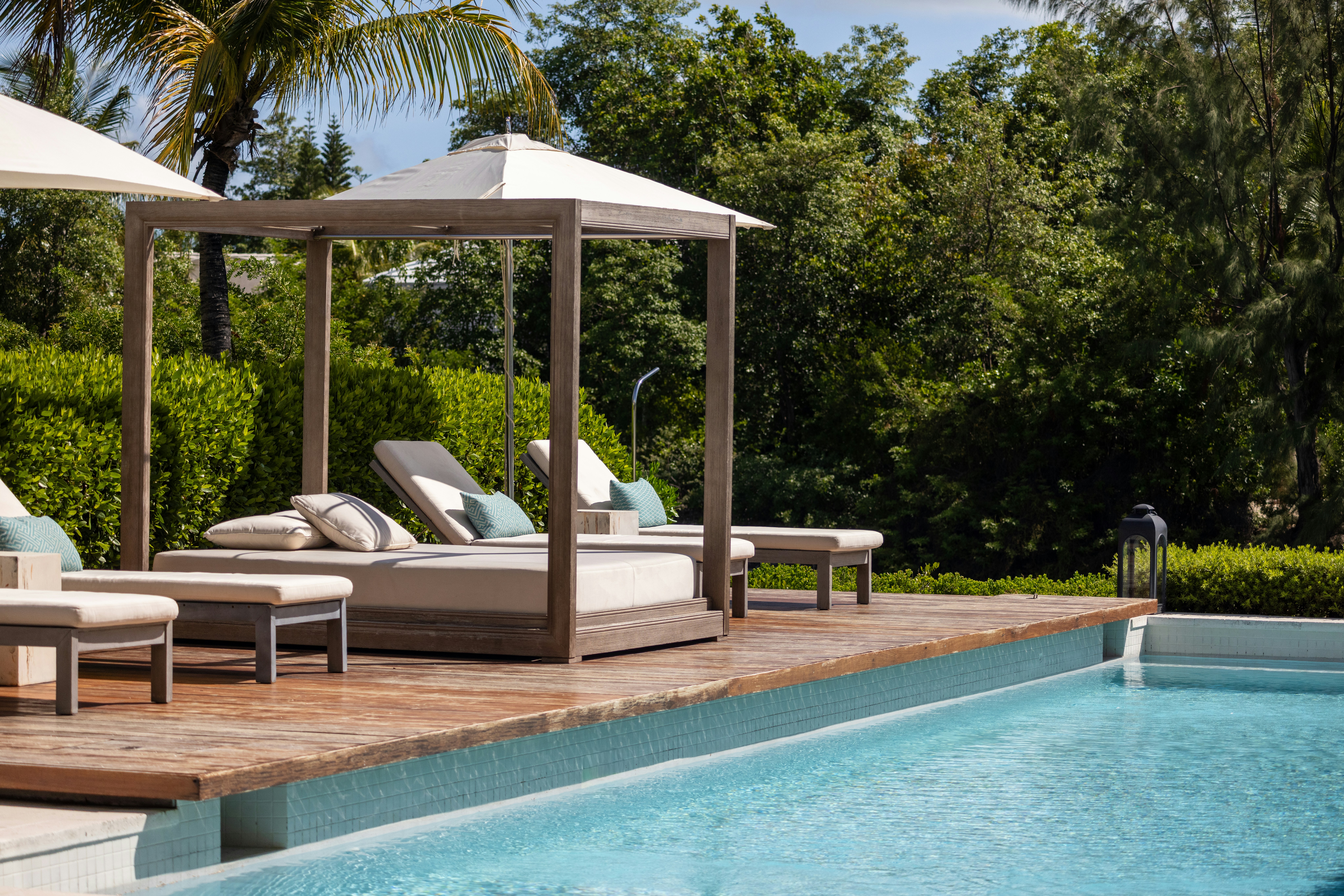 A wooden cabana with beige cushions beside a swimming pool in a garden