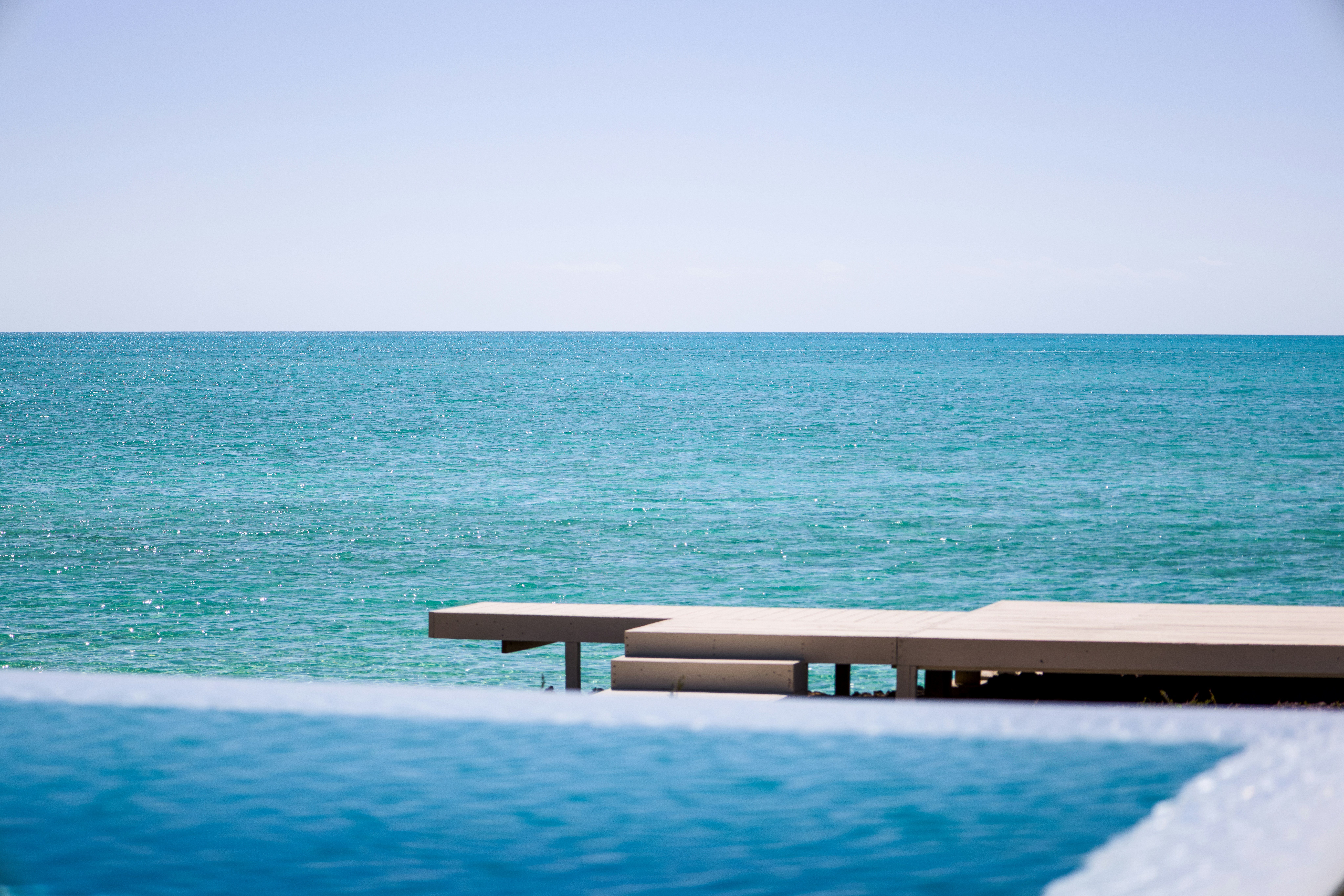 A wooden deck extending toward the turquoise ocean under a clear blue sky