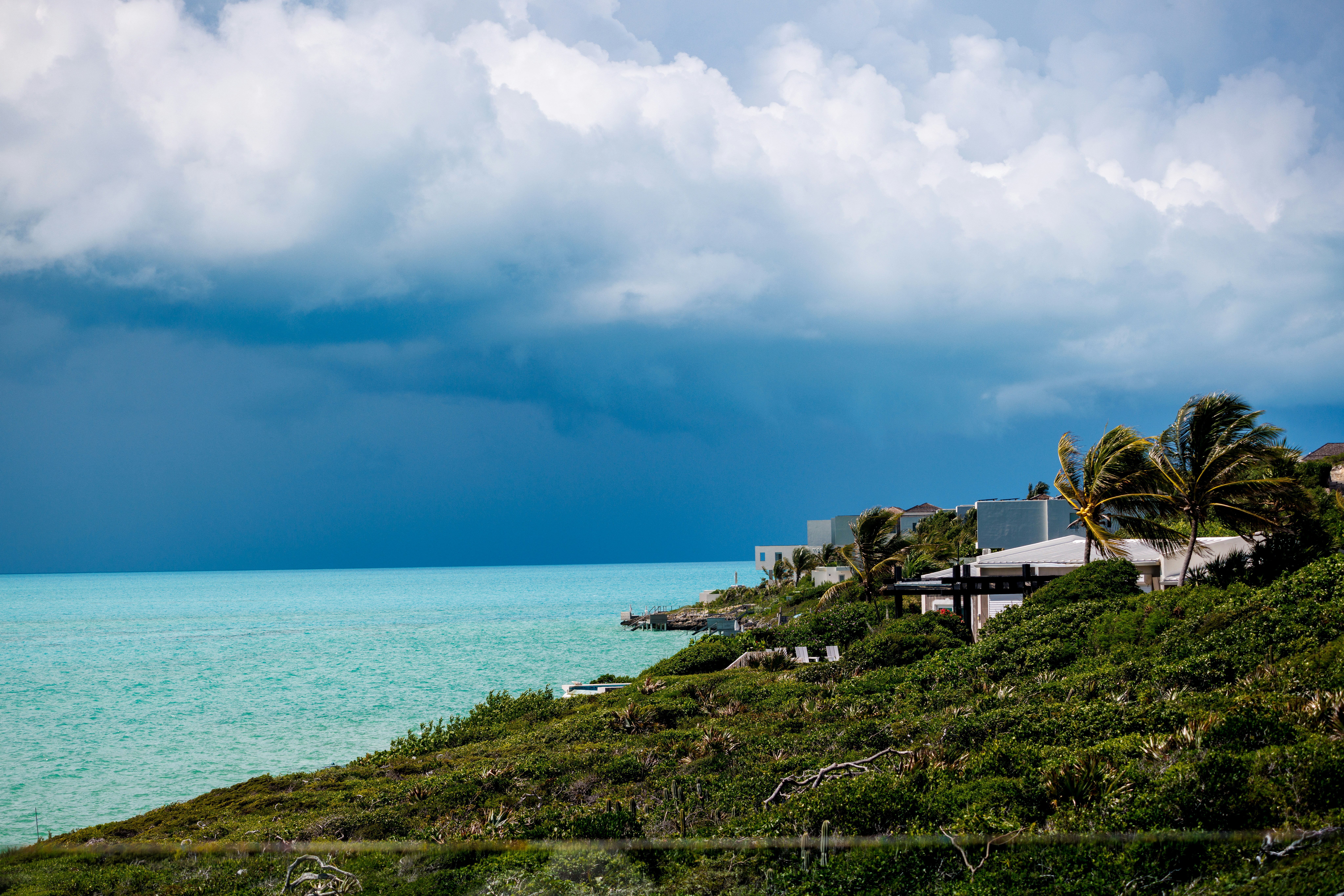 A turquoise sea under a dark storm cloud beside a green coastal hillside