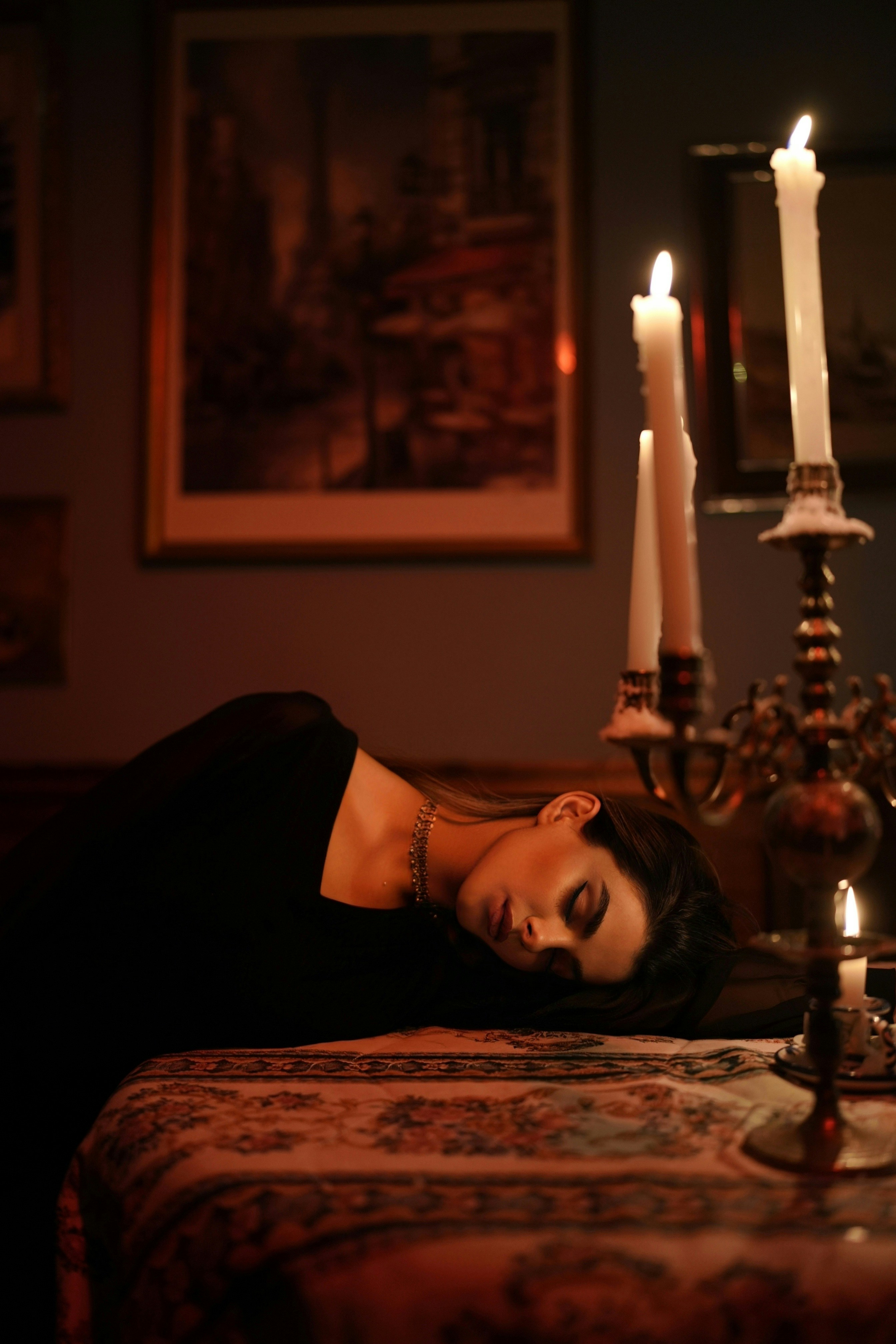 Una donna in abito nero che riposava su un tavolo accanto a un candelabro