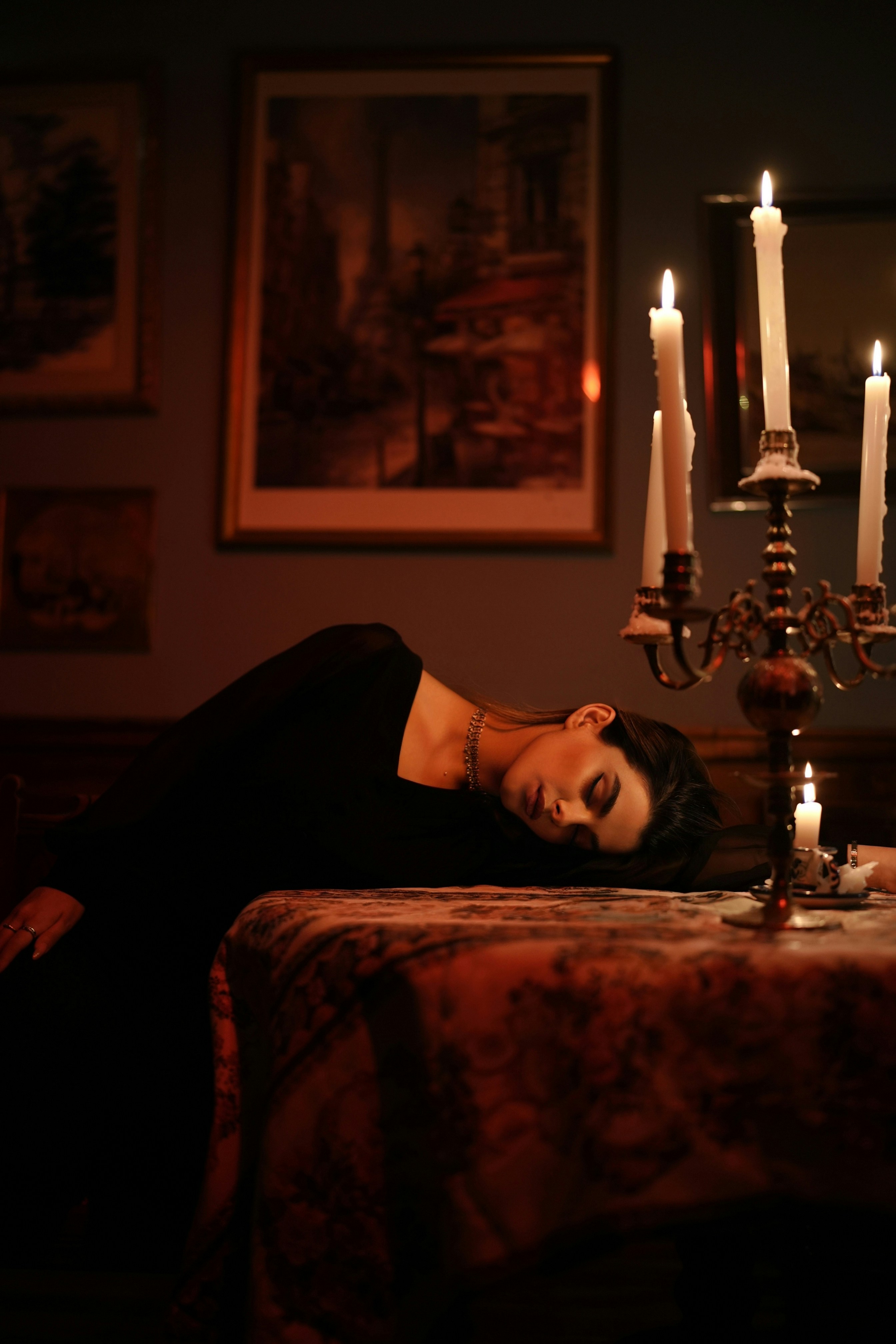 Una donna in abito nero che riposava su un tavolo accanto a un candelabro