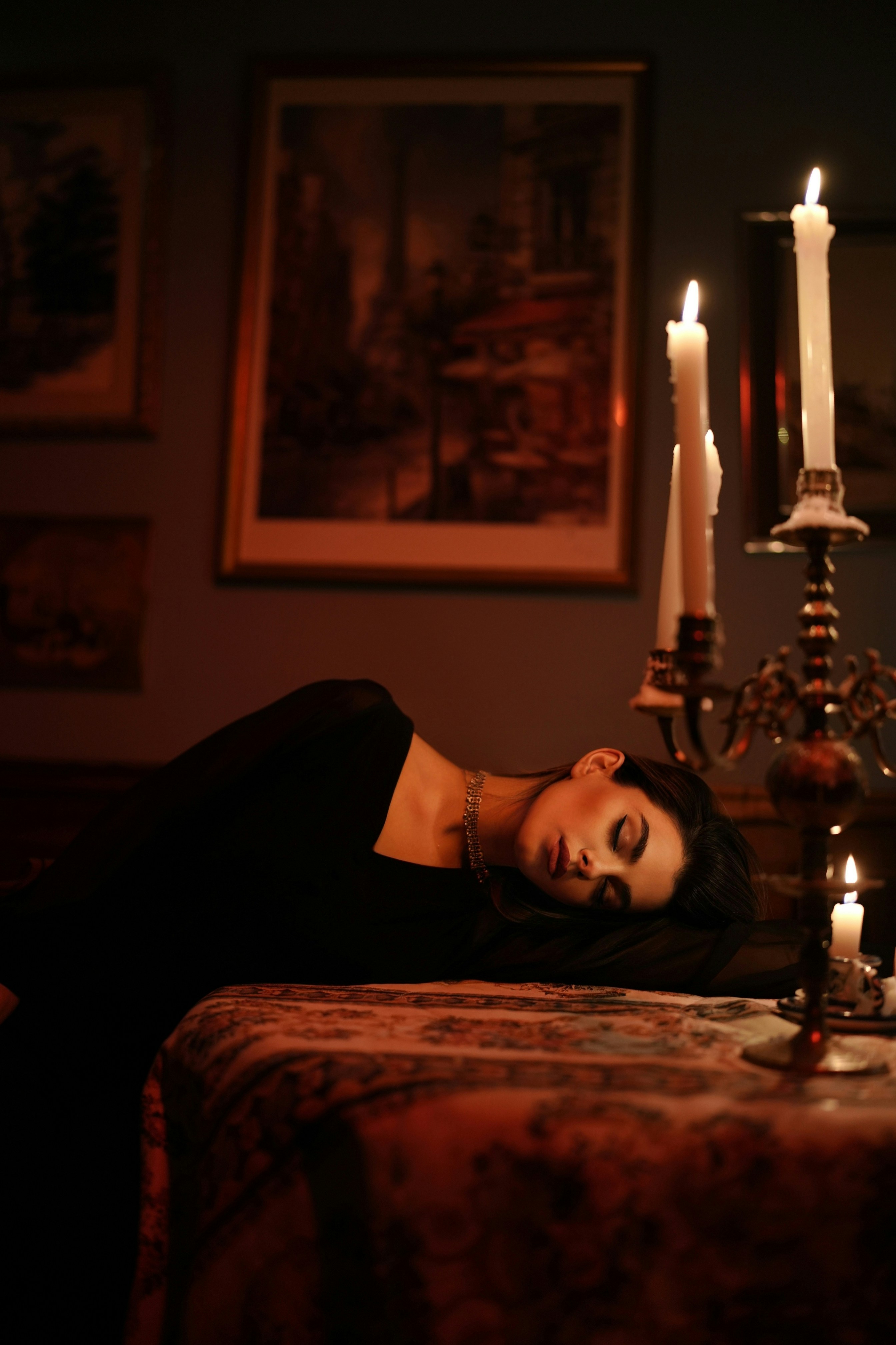 Una donna in abito nero che riposava su un tavolo accanto a un candelabro