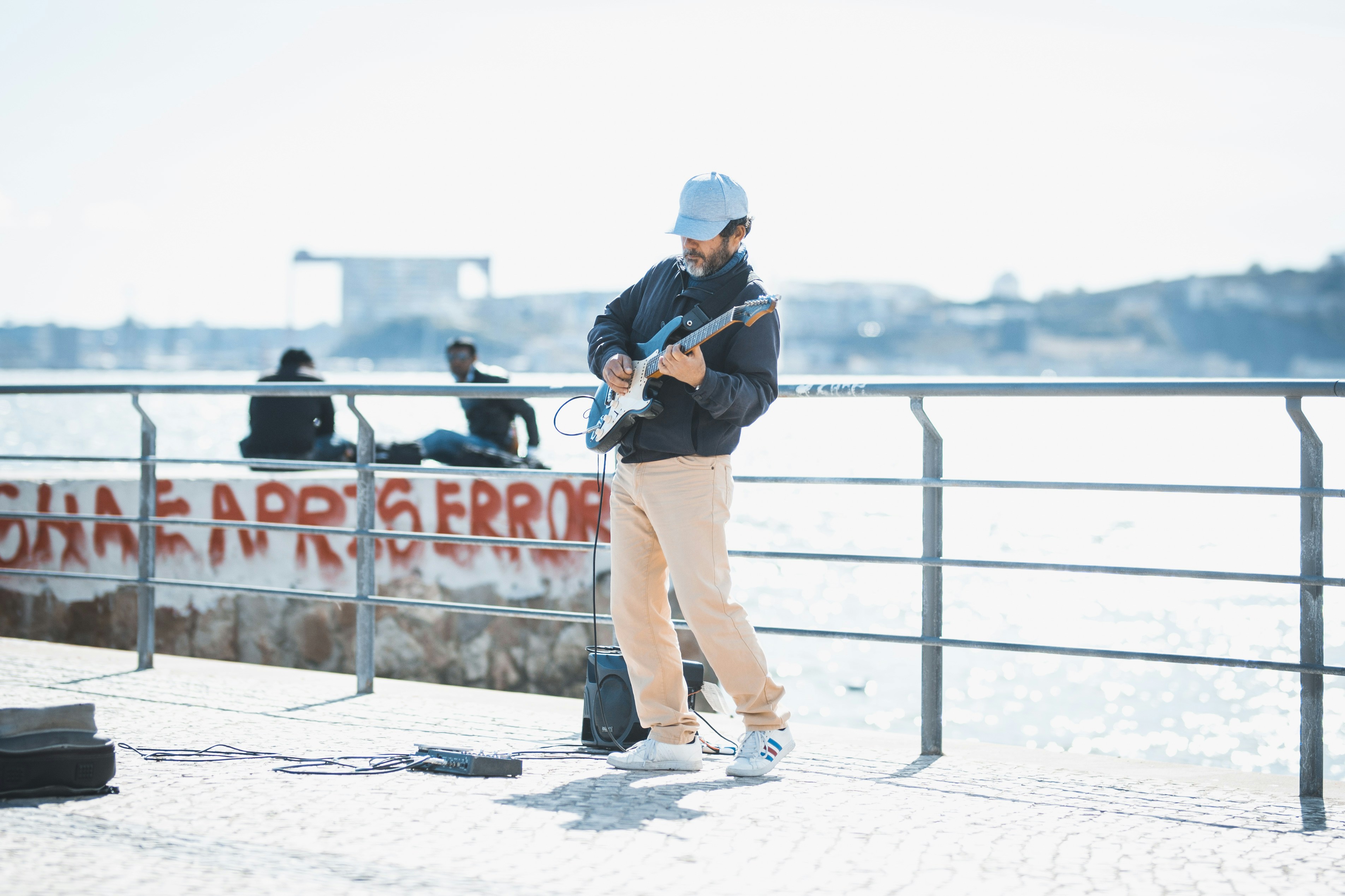 Un homme en casquette bleue jouant de la guitare électrique sur une promenade en bord de mer