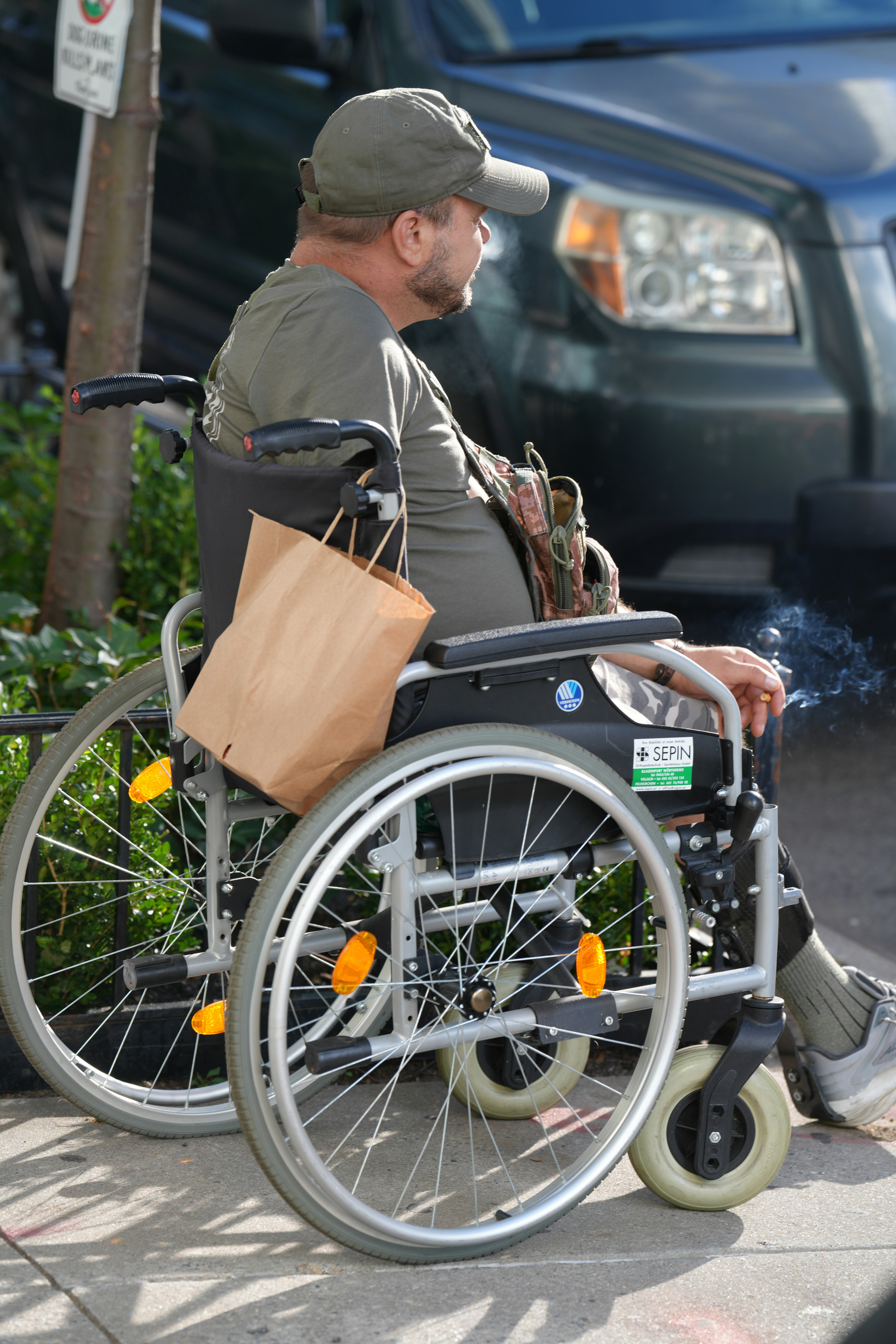 A man in a wheelchair smoking a cigarette on a city sidewalk