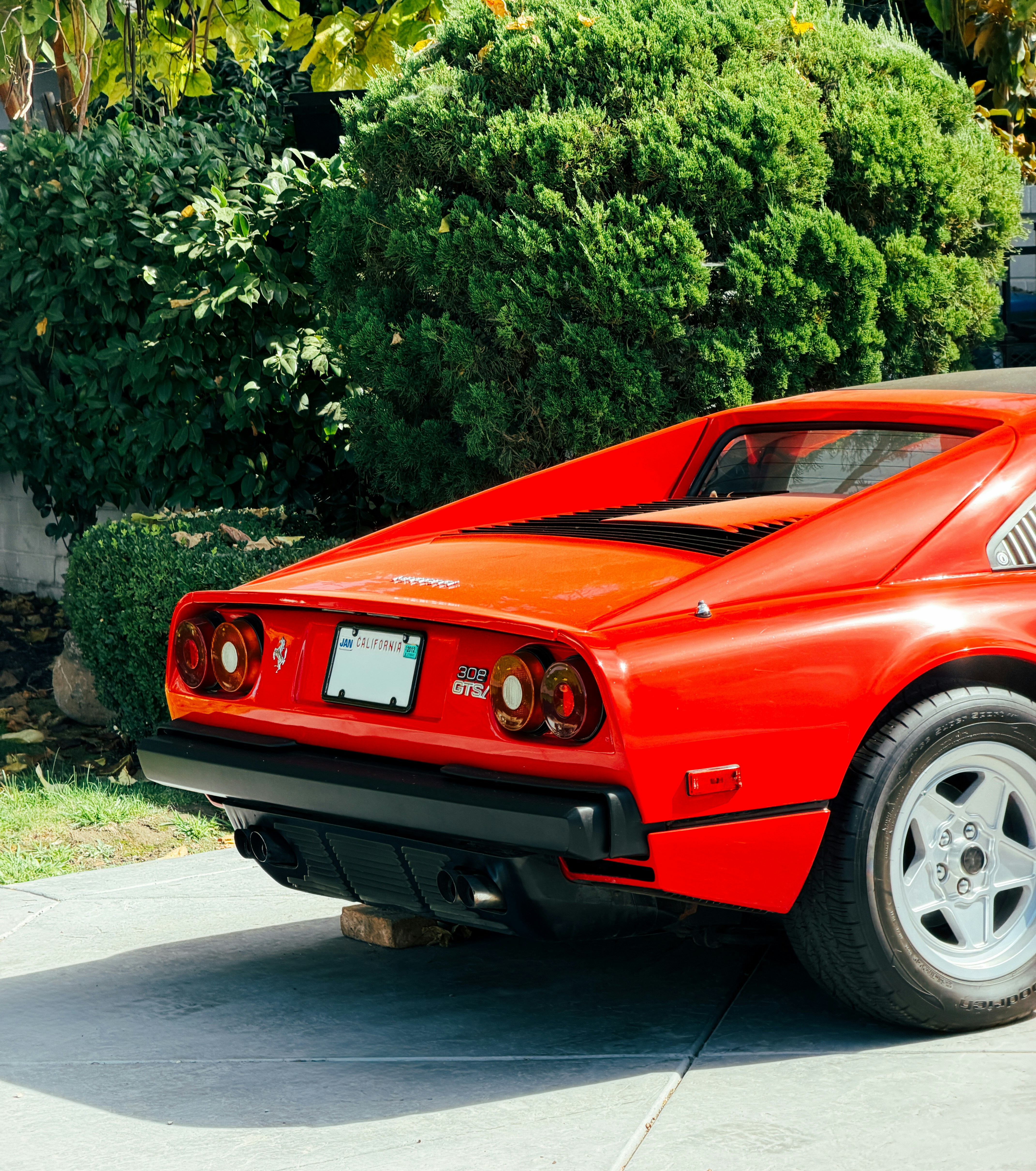 A red sports car parked on a concrete driveway in front of green bushes
