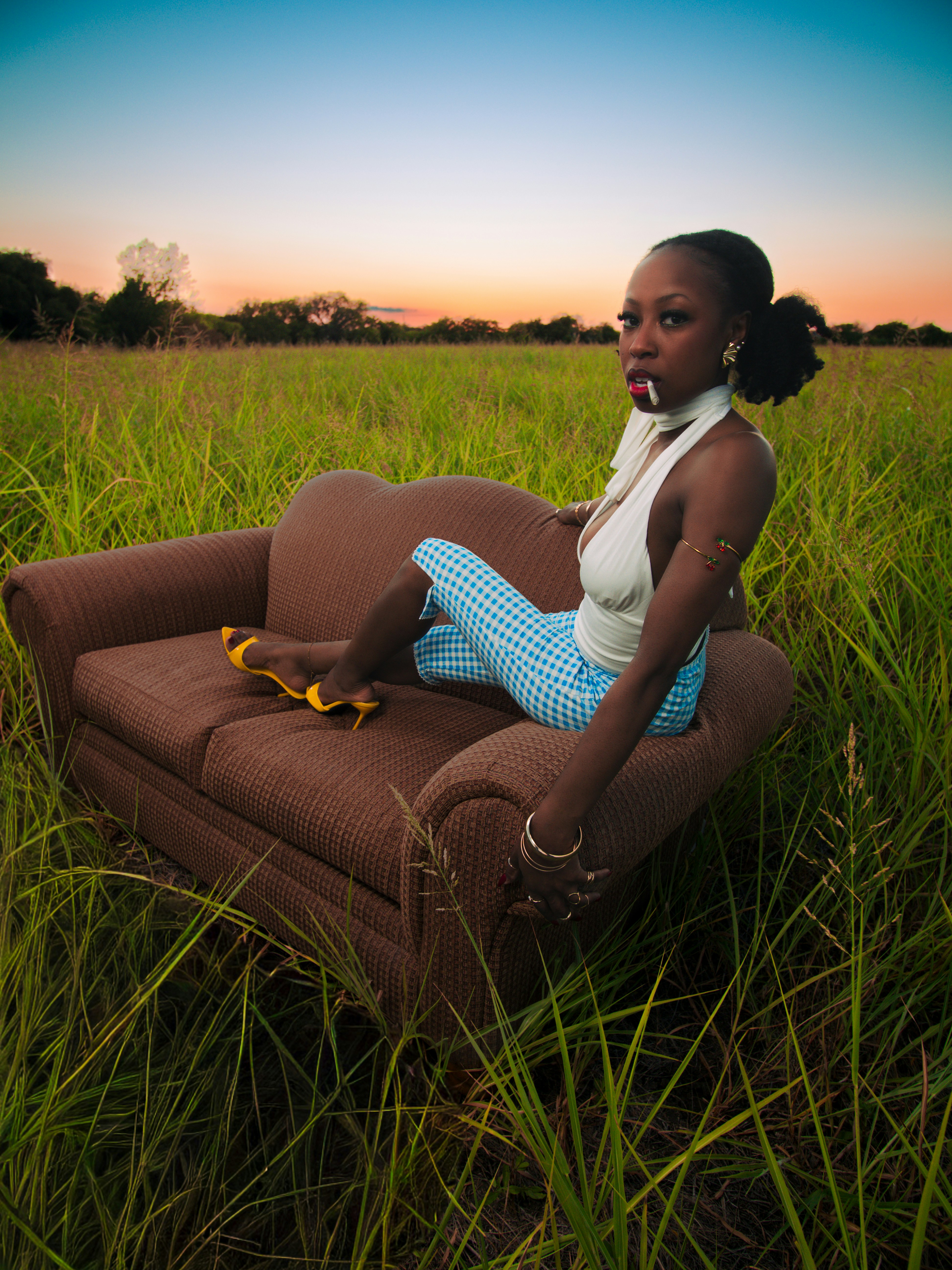 A woman on a brown couch in a grassy field under a warm orange sky
