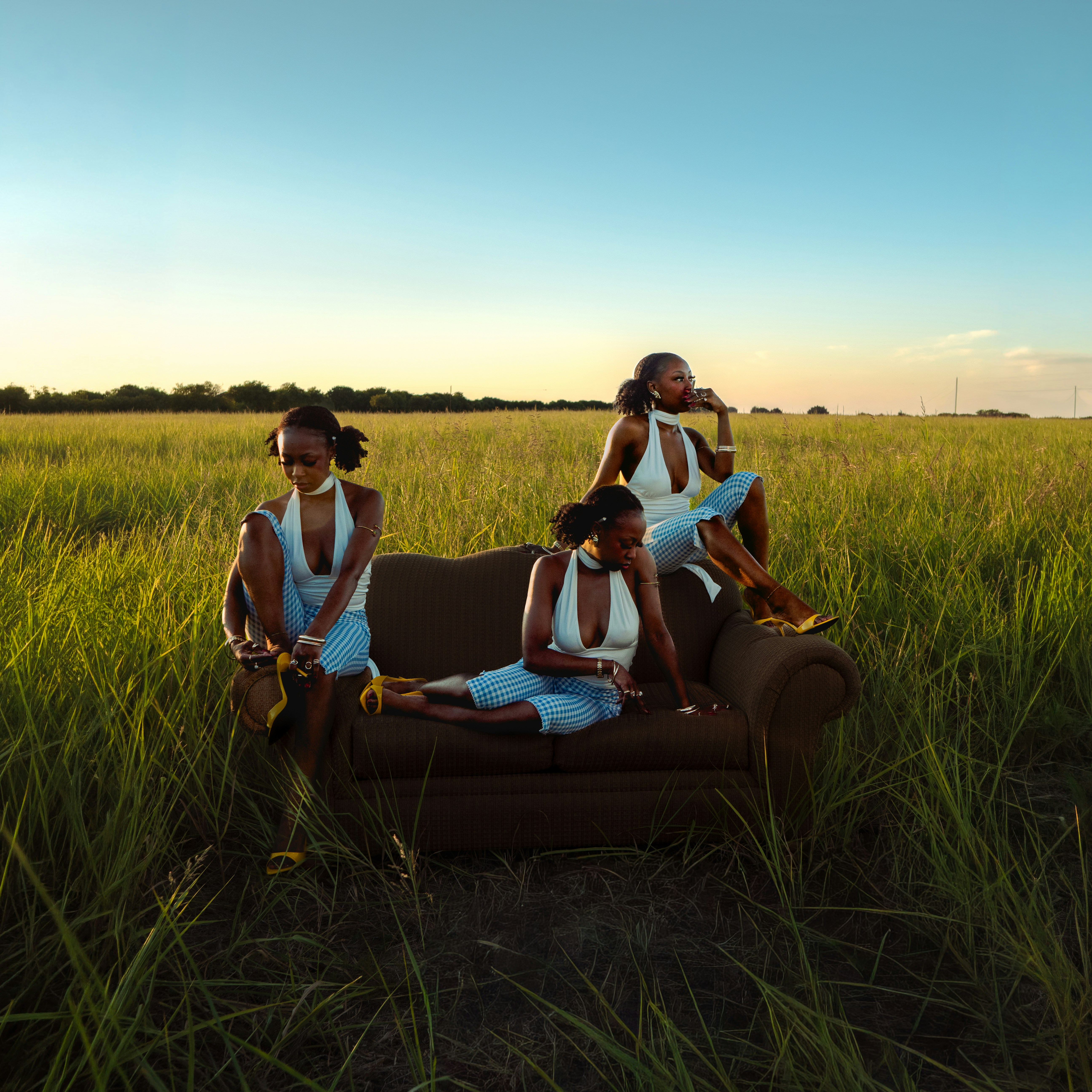 Three versions of the same woman on a brown sofa in a grassy field