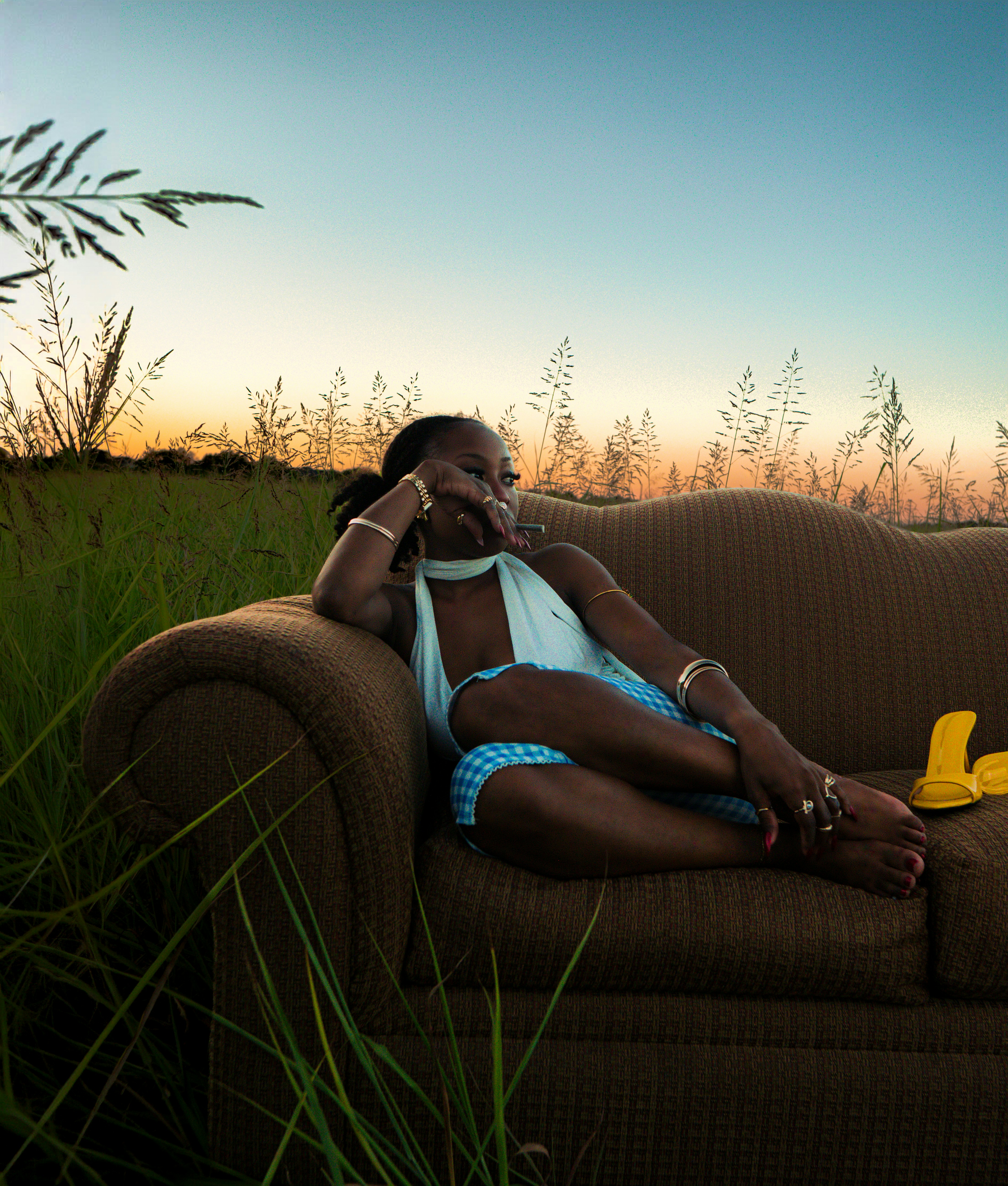 A woman on a brown couch in a field against a warm orange sky