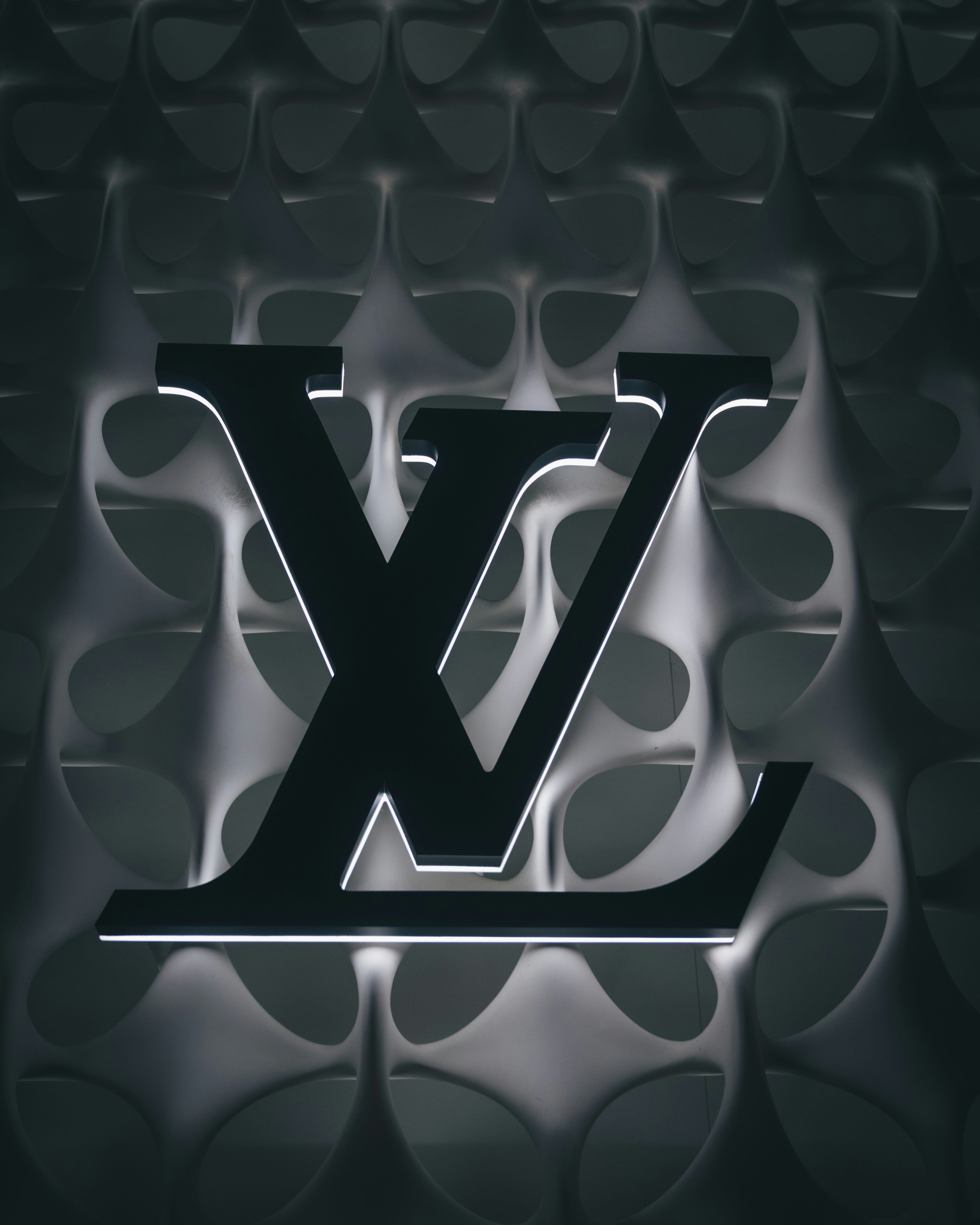 A backlit Louis Vuitton logo mounted on a white geometric lattice wall
