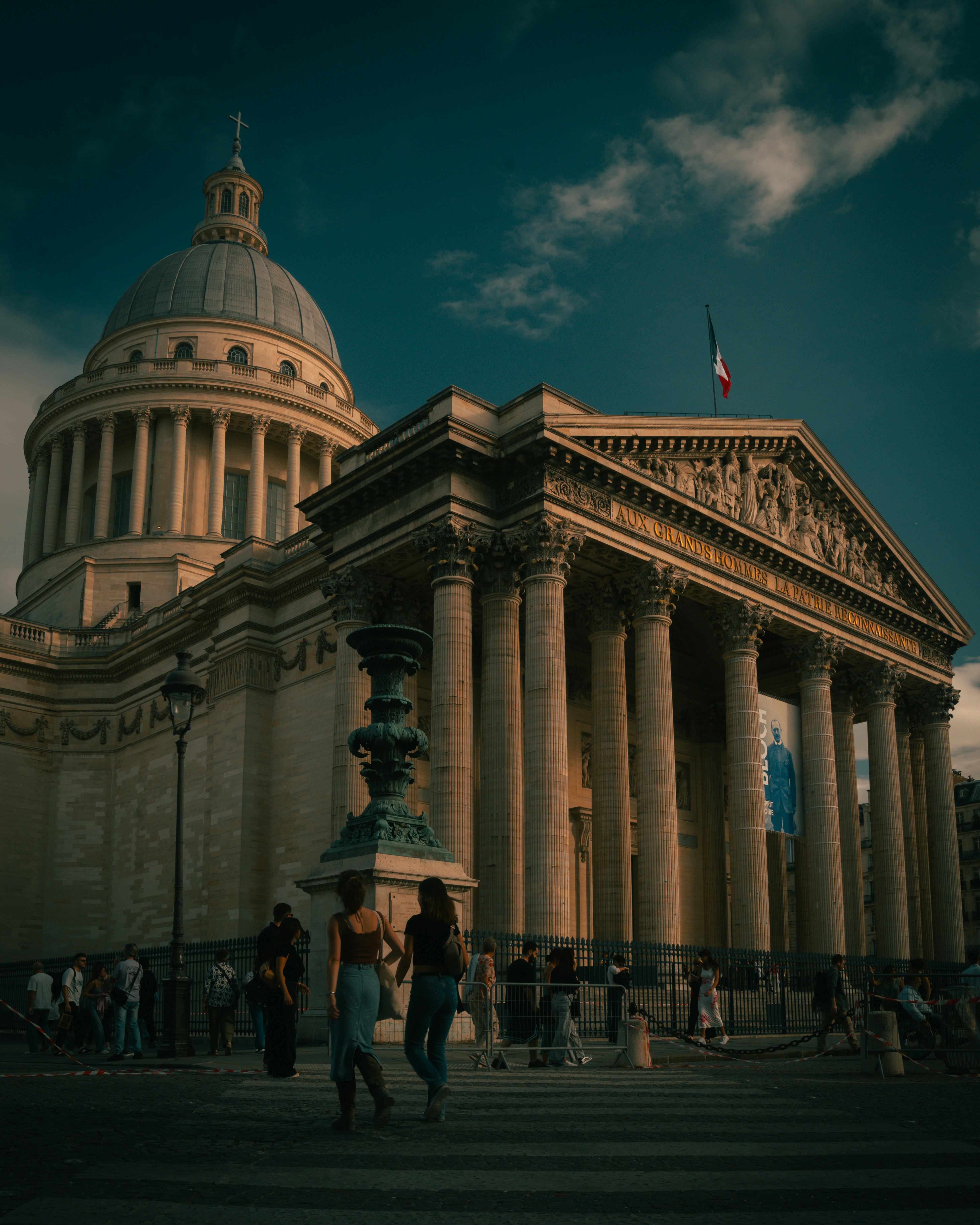 People walking past the Pantheon in Paris under a dark blue sky
