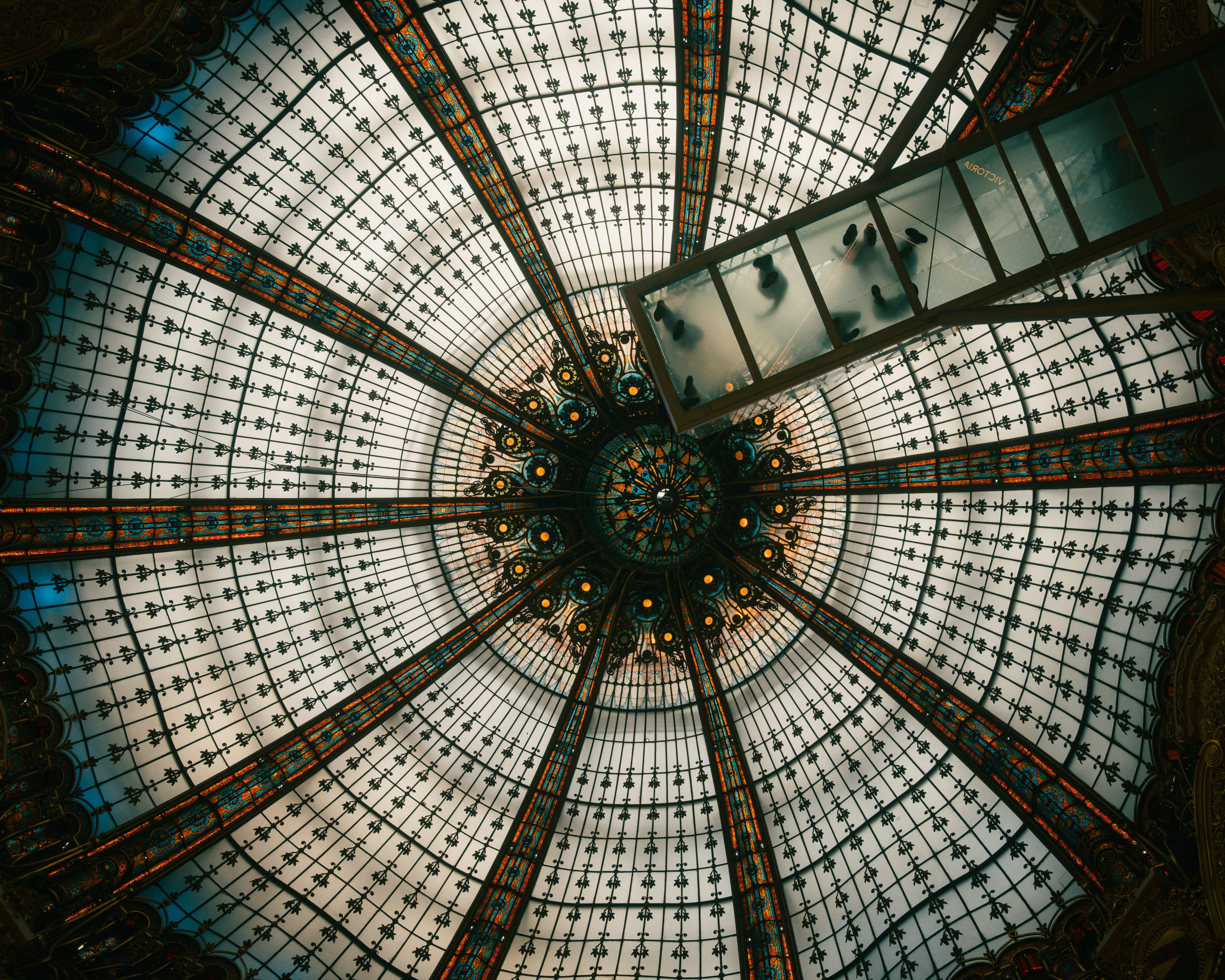 A glass dome with intricate metal patterns and a glass walkway with people