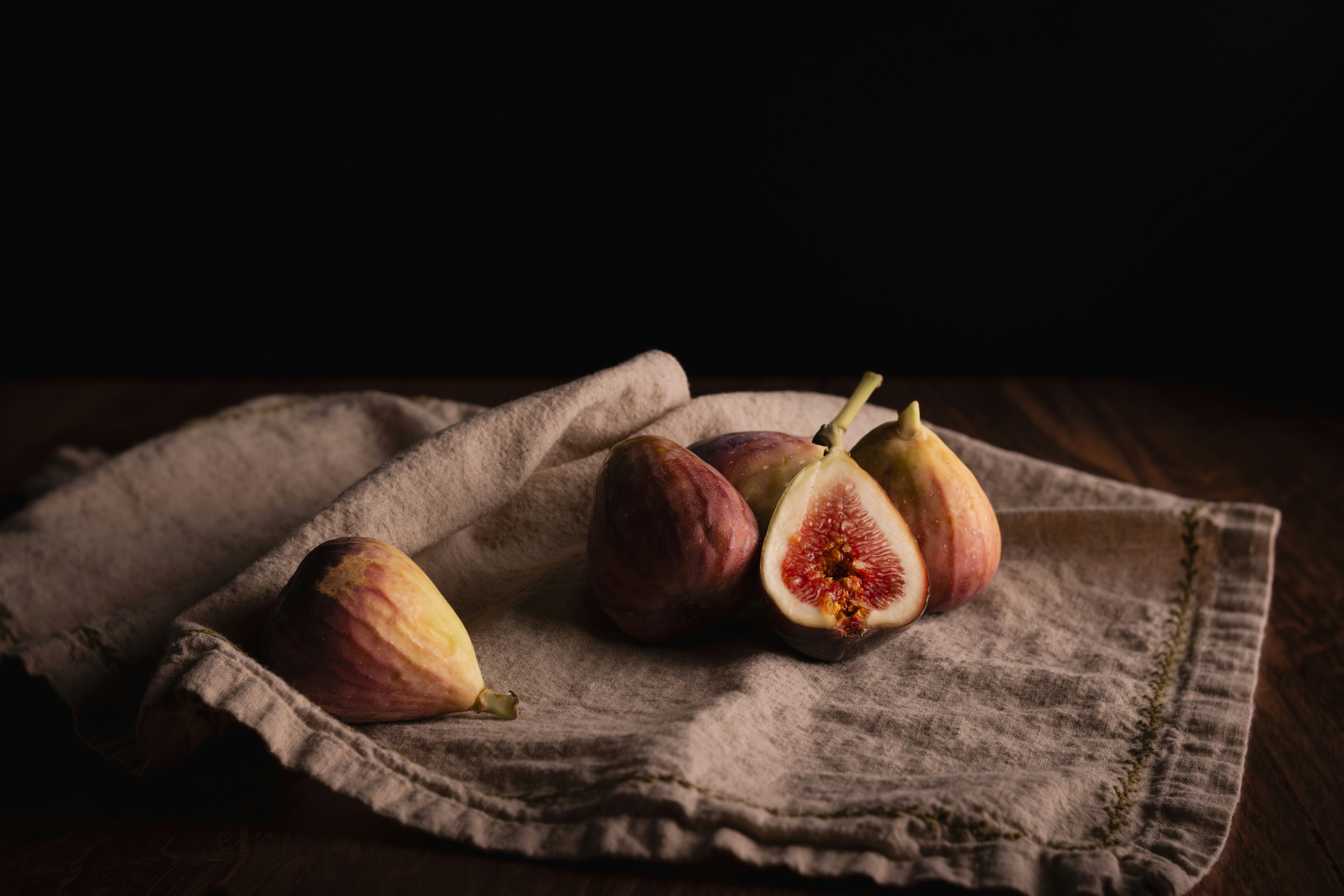 Whole and halved figs on a beige linen cloth against a dark background
