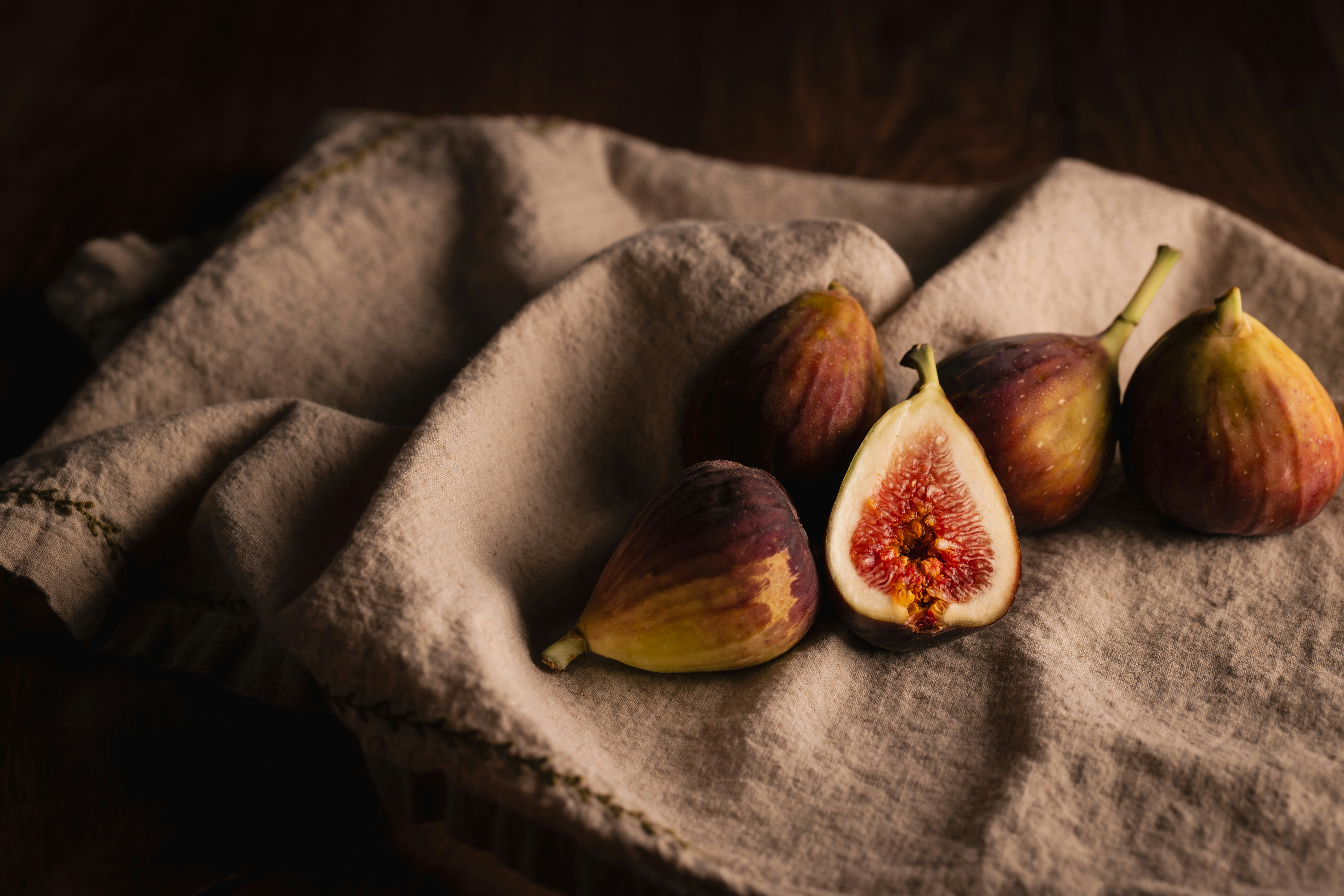 Four whole and halved figs on a textured beige linen cloth