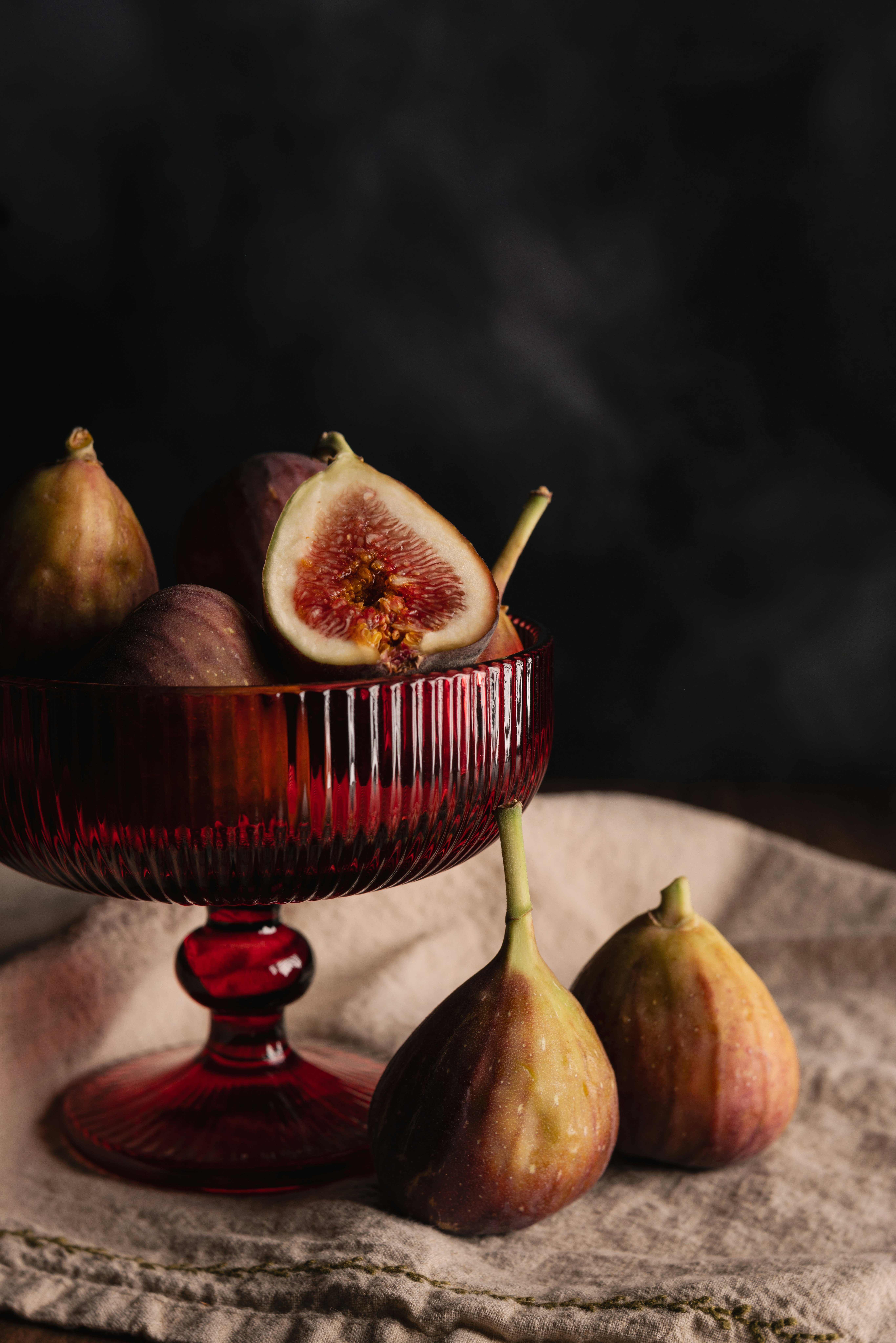 Fresh figs in a red glass pedestal bowl on a beige linen cloth