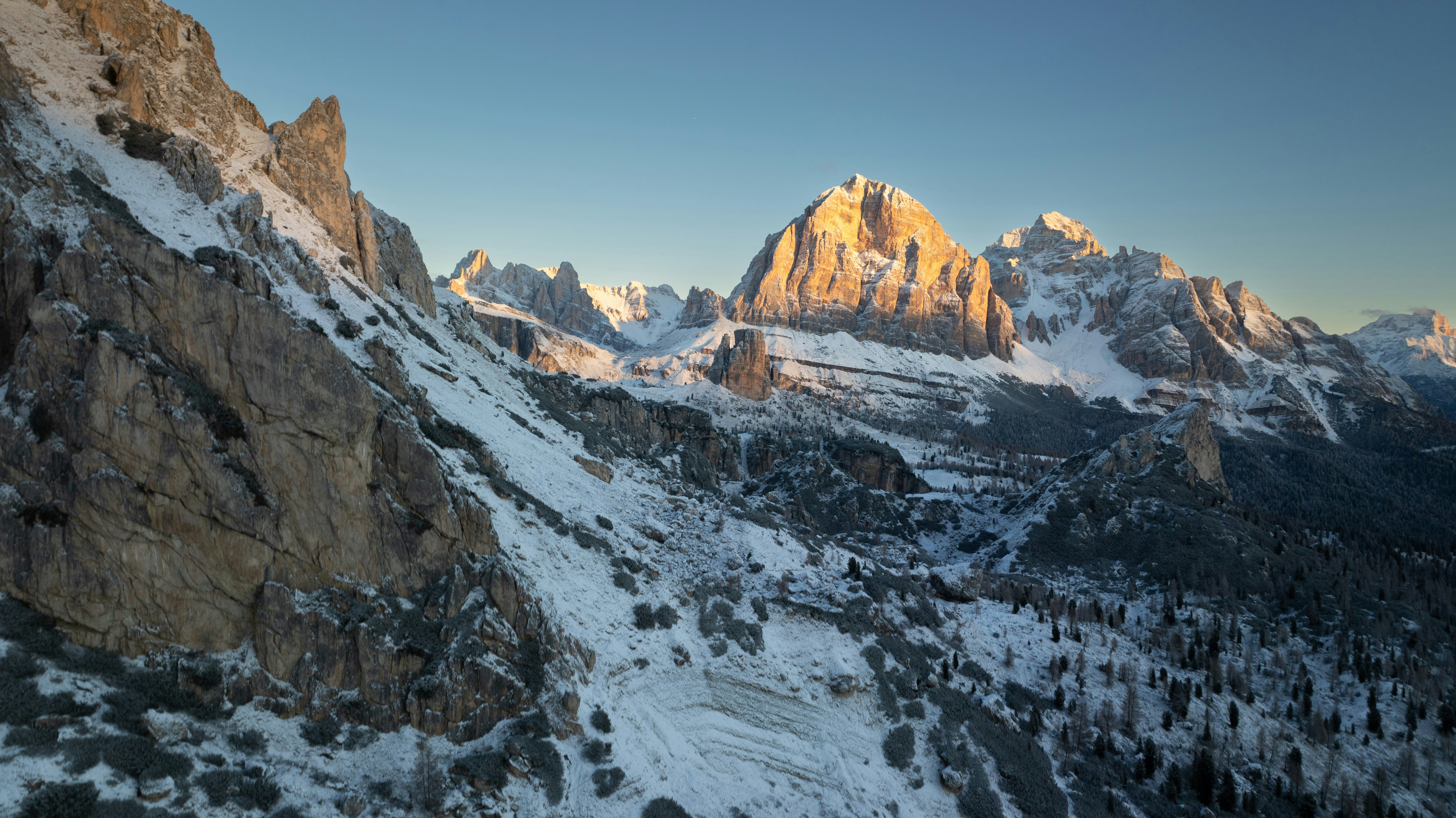Snowy mountain peaks illuminated by low golden light above a forested valley
