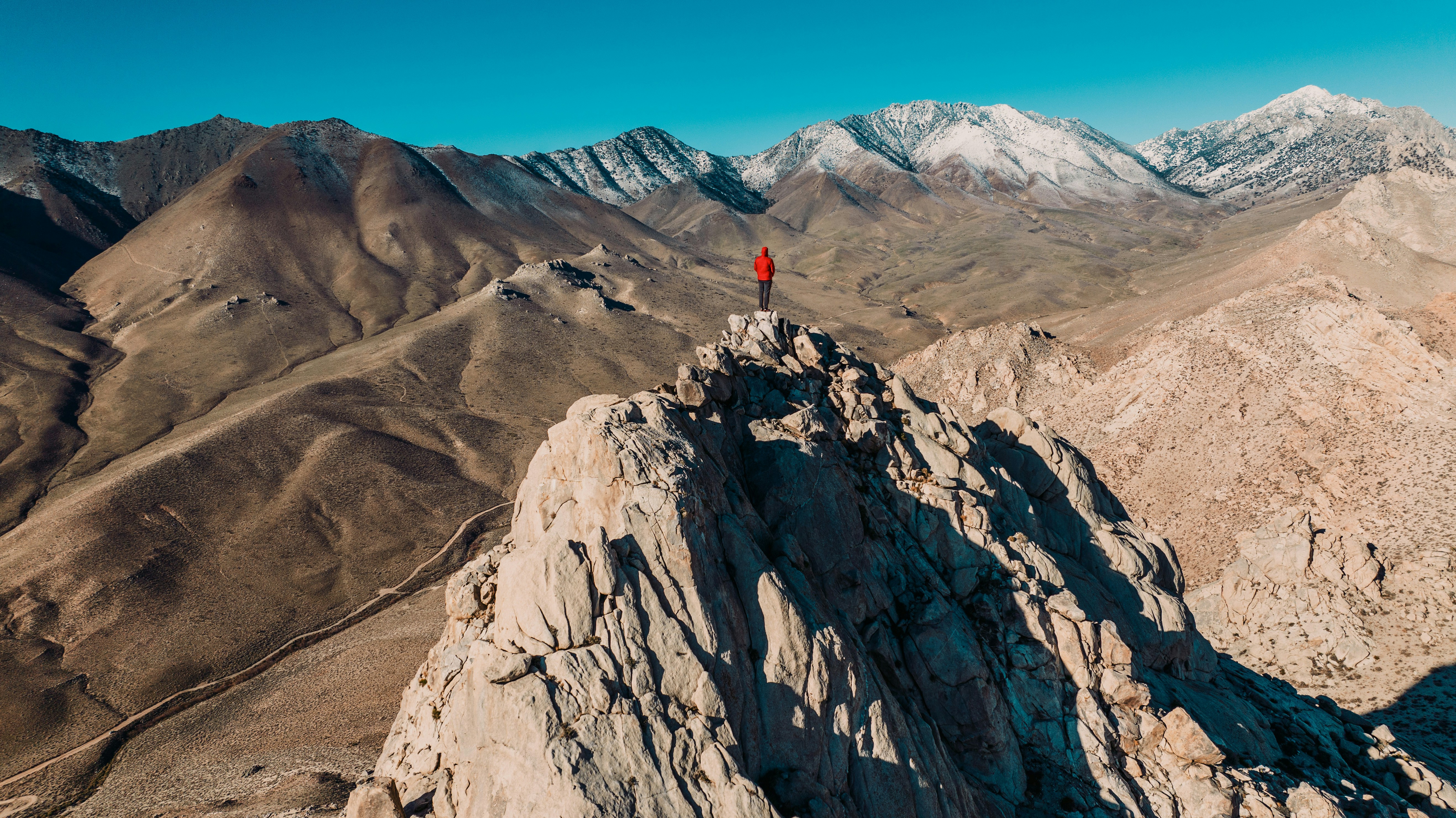 A person in a red jacket on a rocky peak overlooking snowy mountains