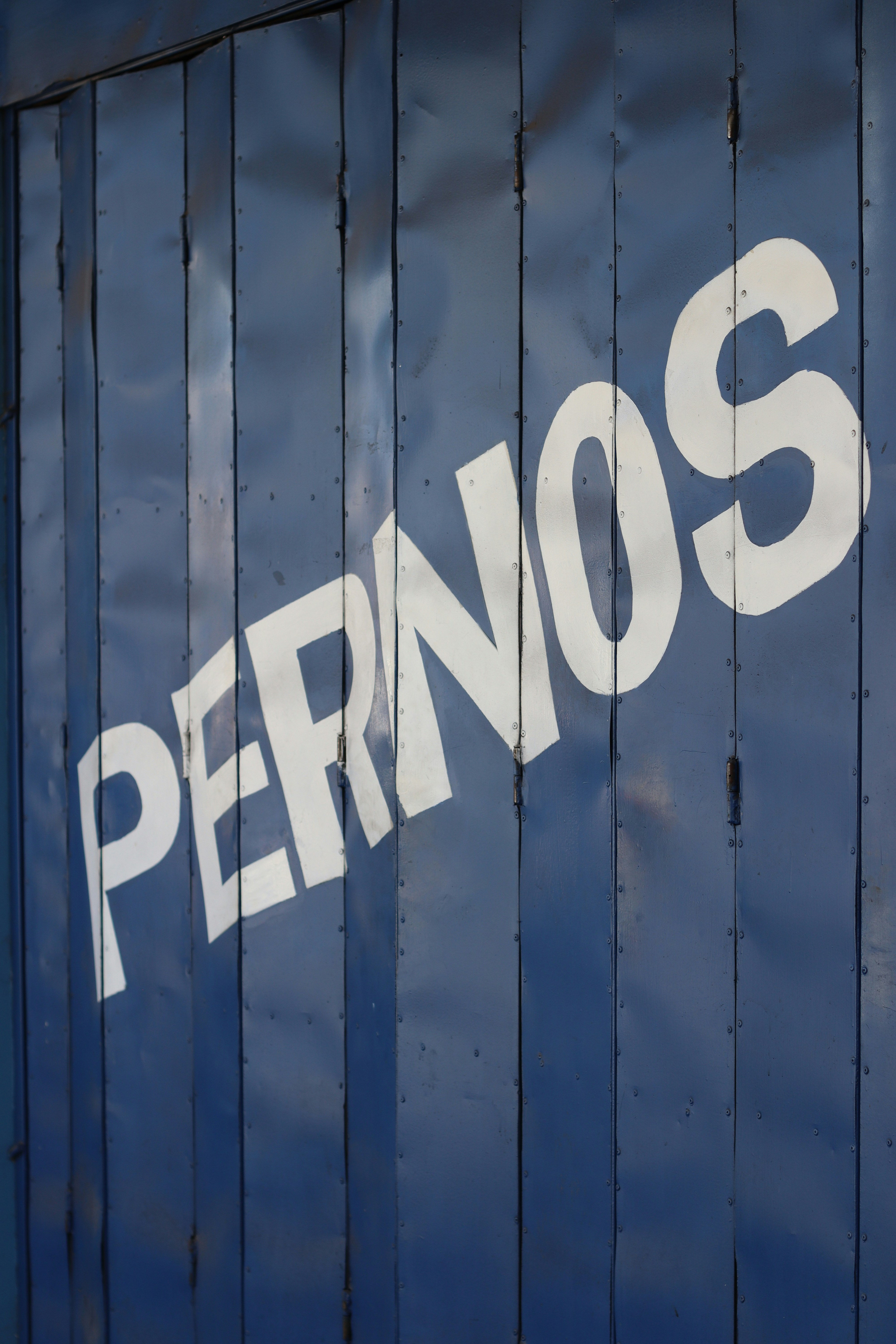 White text reading PERNOS painted diagonally on a dark blue metal folding door