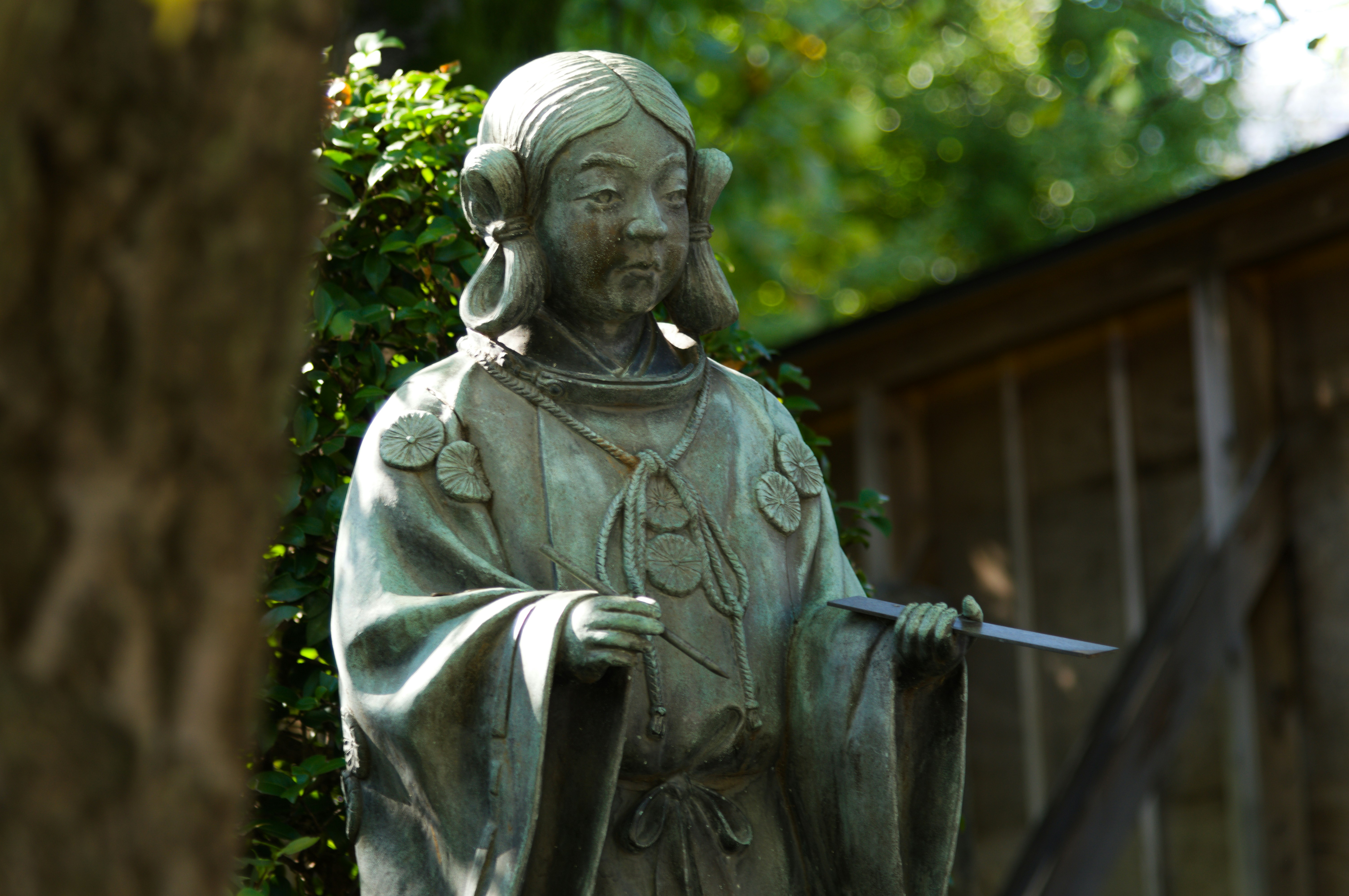 A weathered bronze statue of a person in traditional robes holding a thin blade