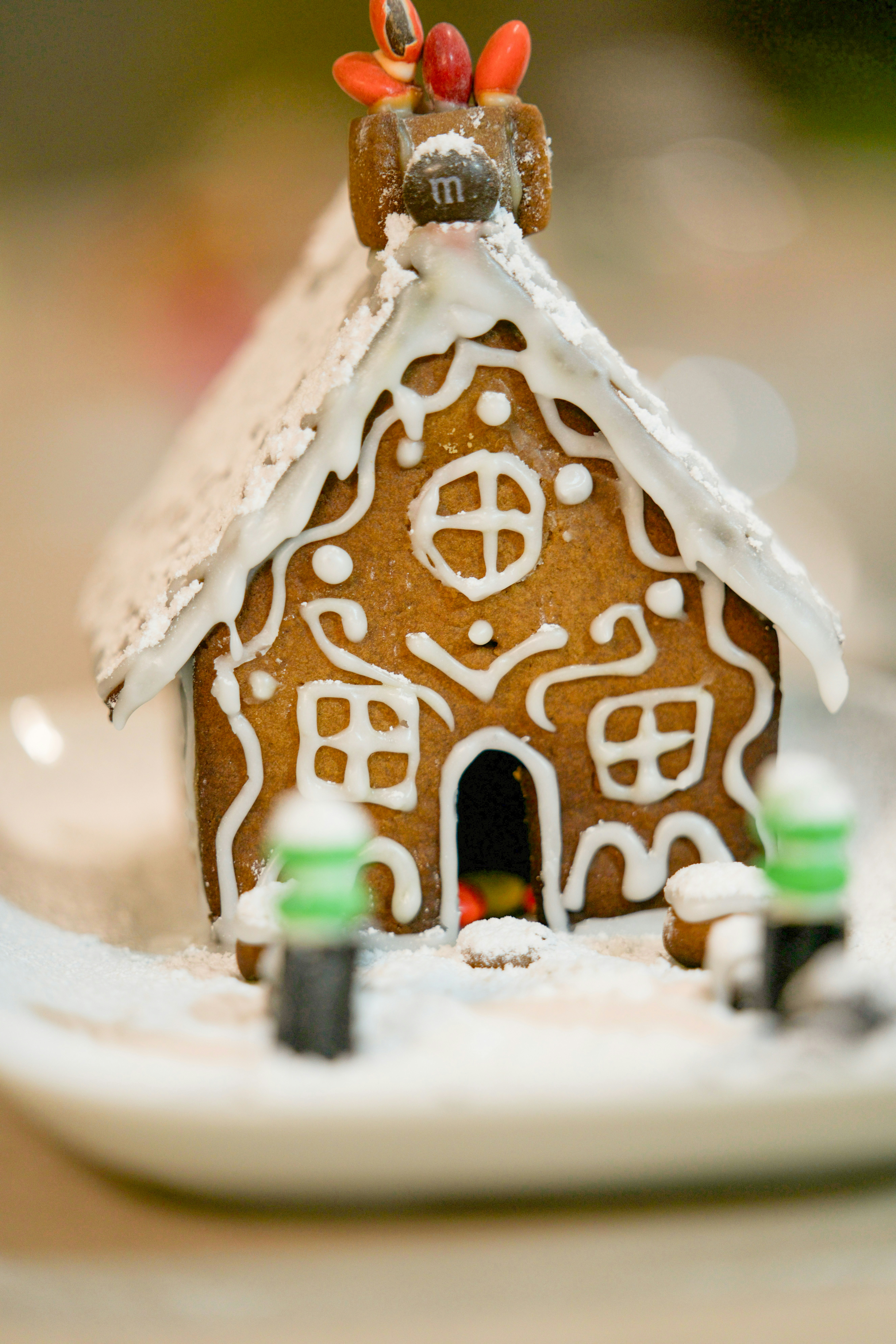 A small gingerbread house decorated with white icing on a white plate