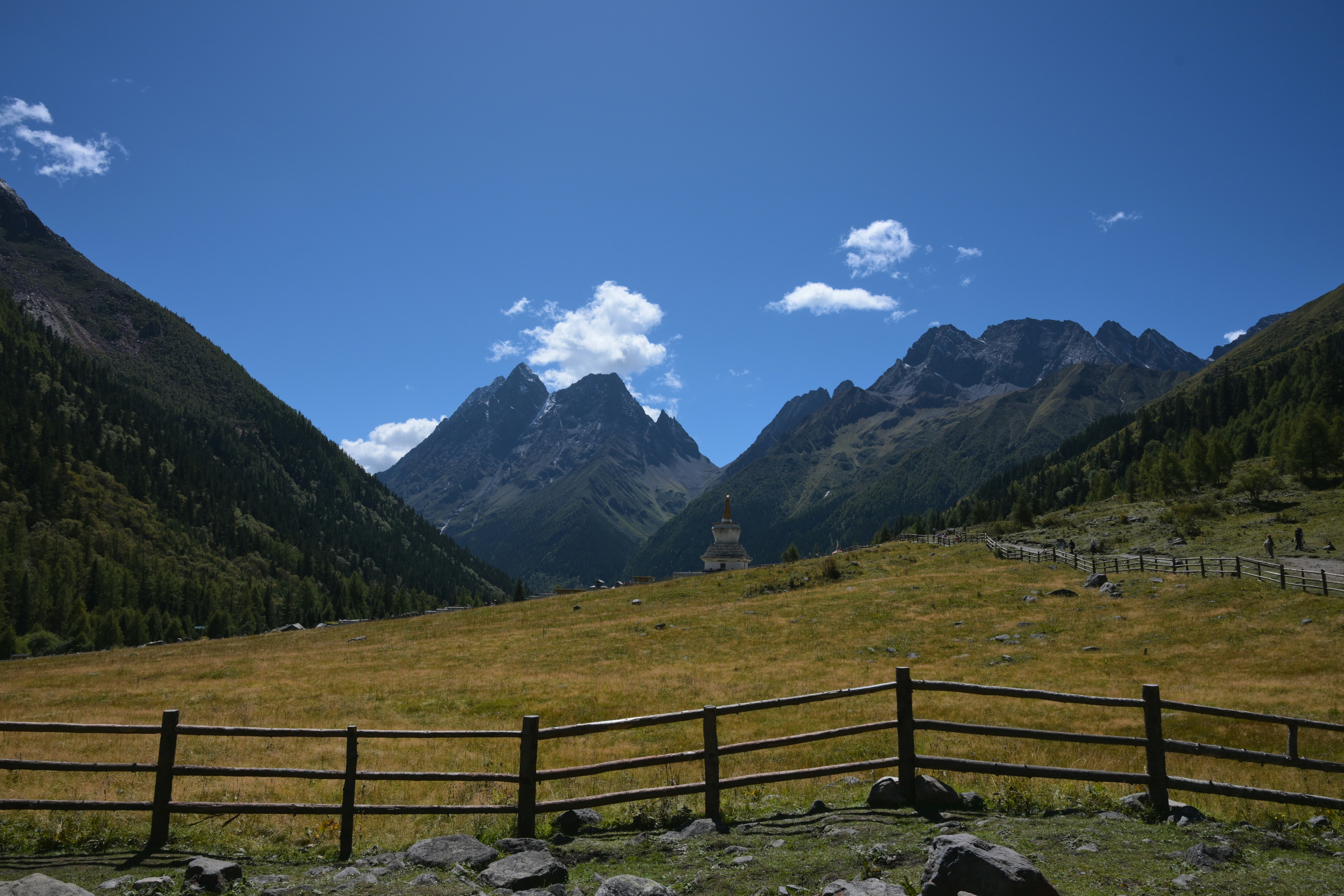 A white stupa in a grassy mountain valley under a clear blue sky
