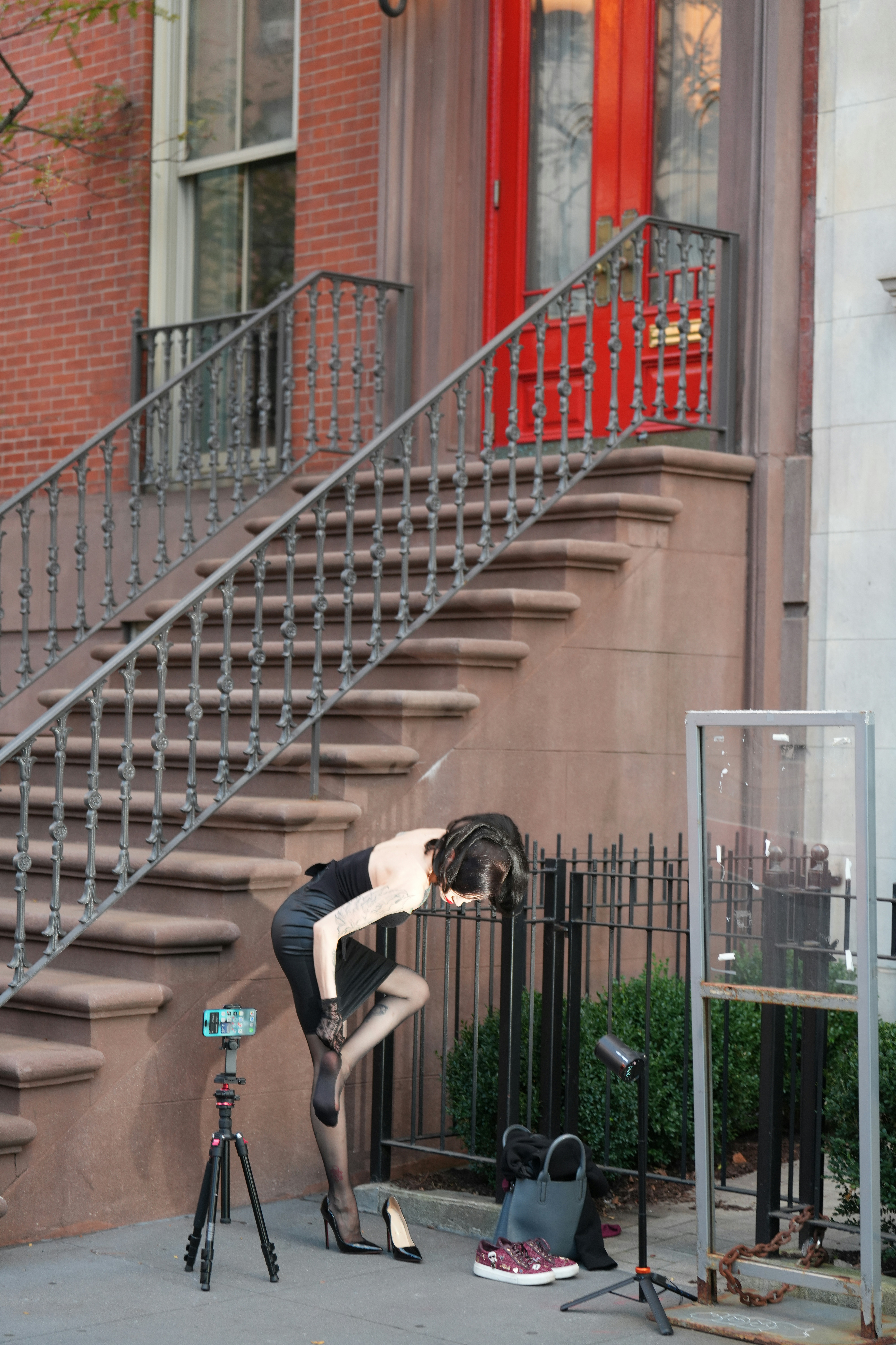 A person in a black dress adjusting stockings on a city sidewalk
