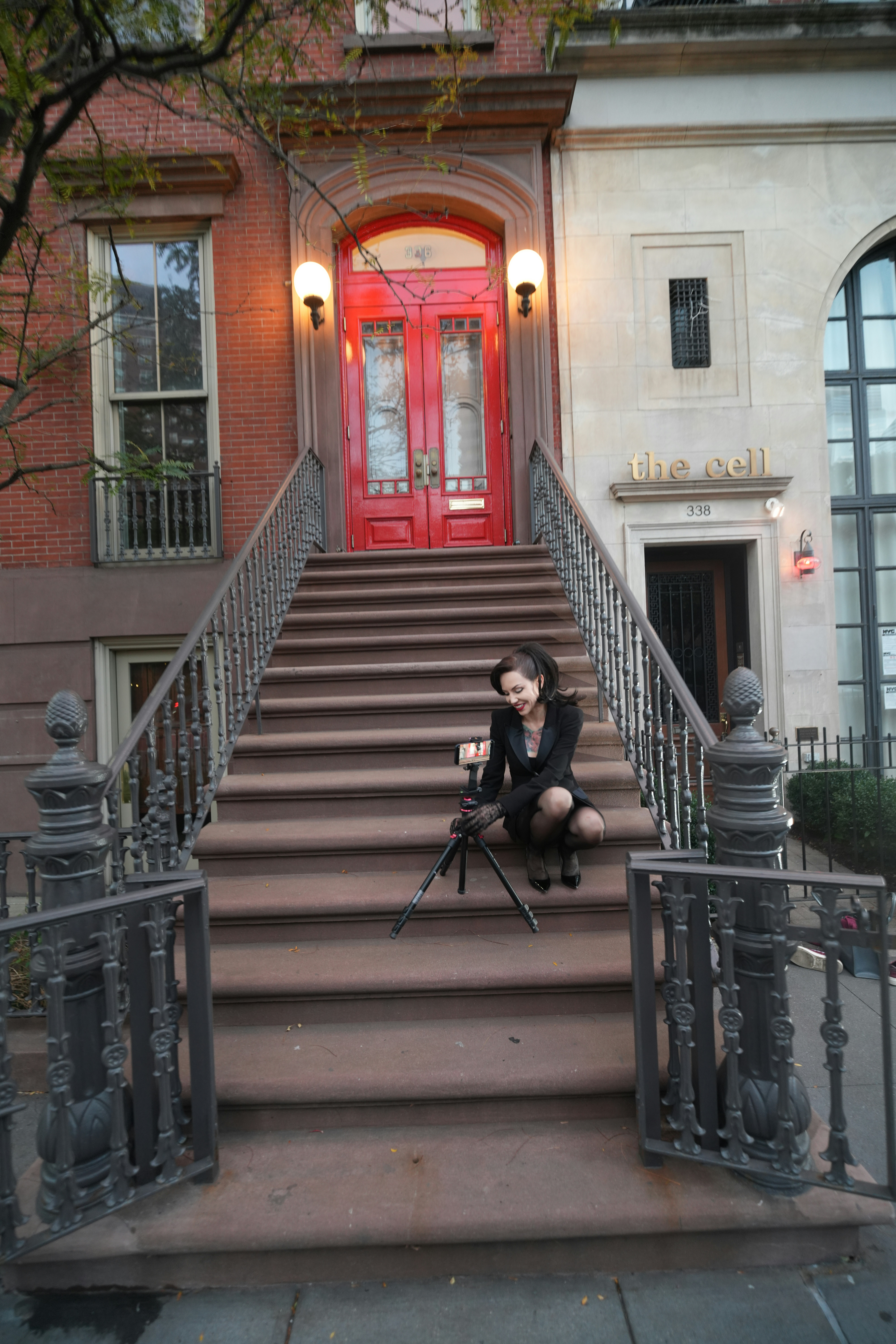 A woman in a black blazer adjusting a camera on a tripod on brownstone steps