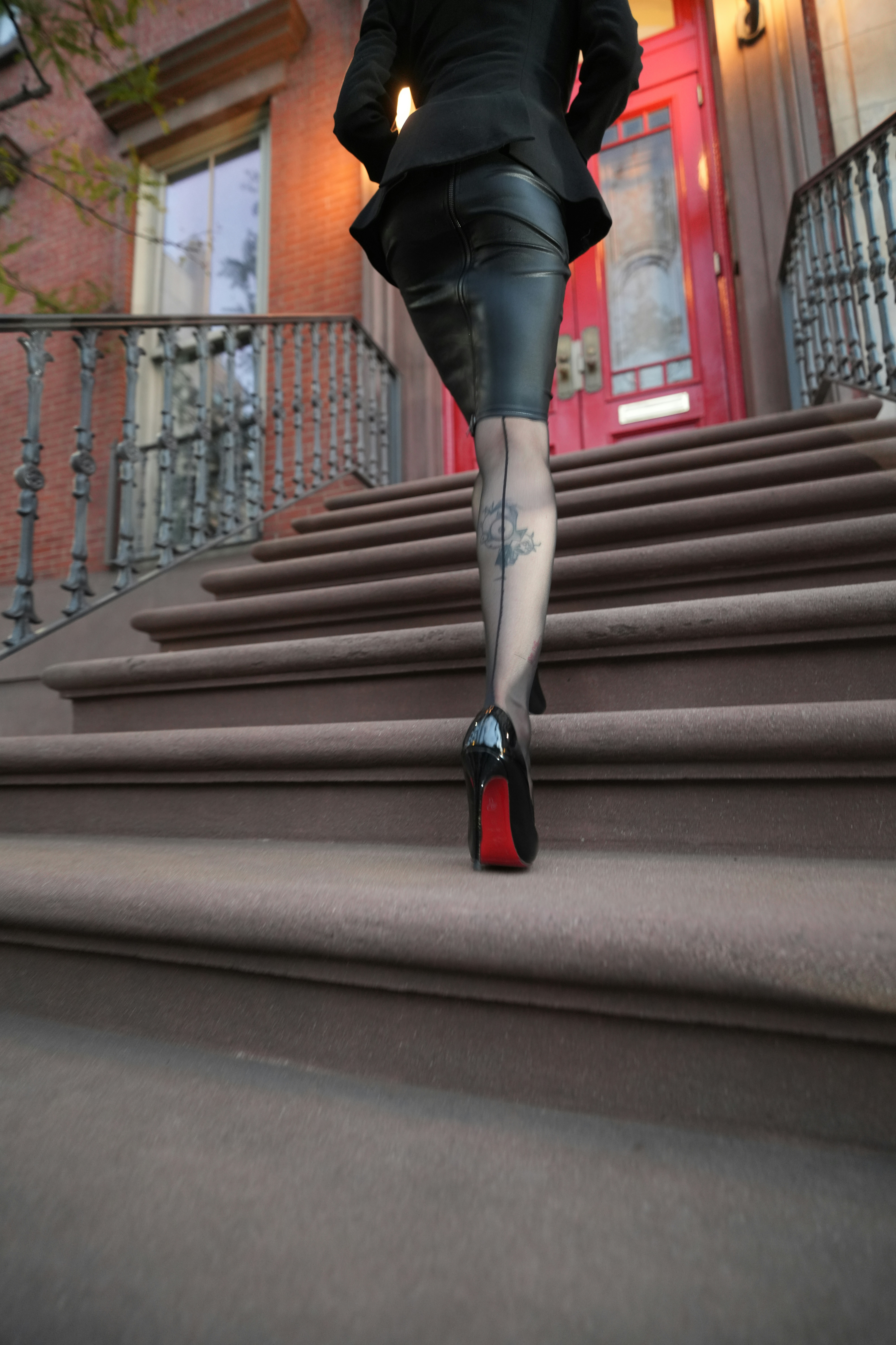A person in a black blazer and leather skirt walking up brownstone steps