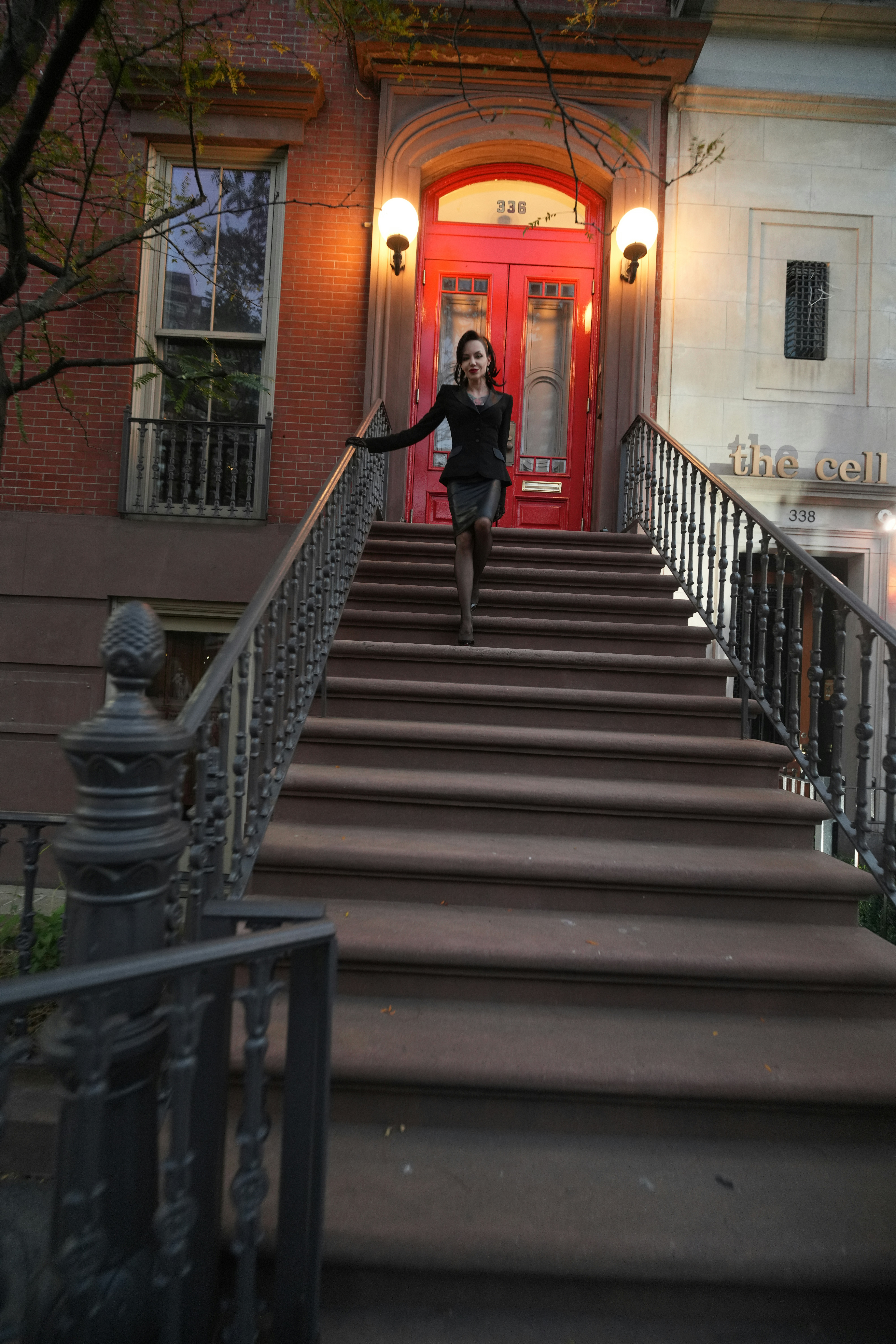 A woman in a black suit descending brownstone steps toward a red door