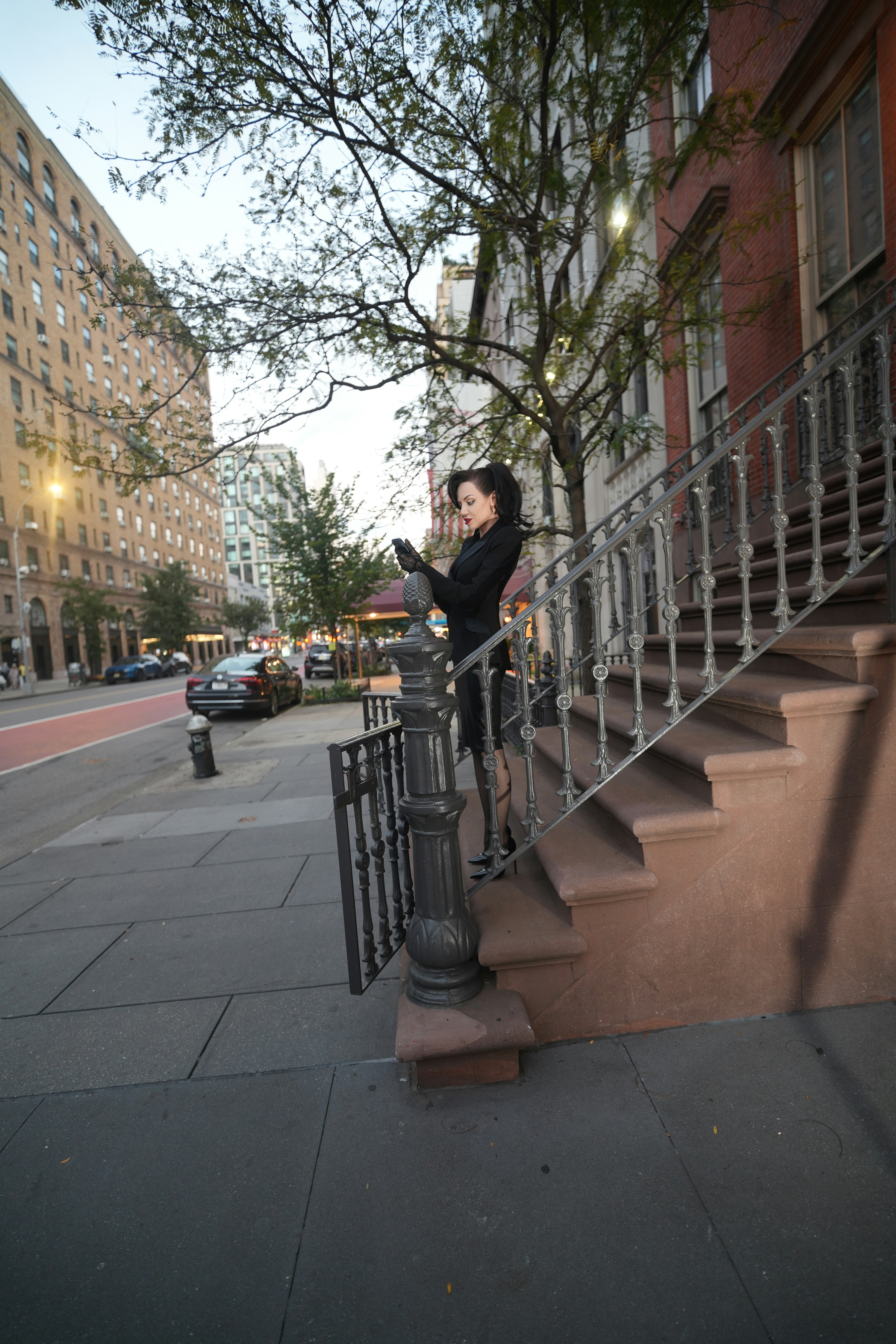 A woman in a black suit using a smartphone on brownstone steps in New York