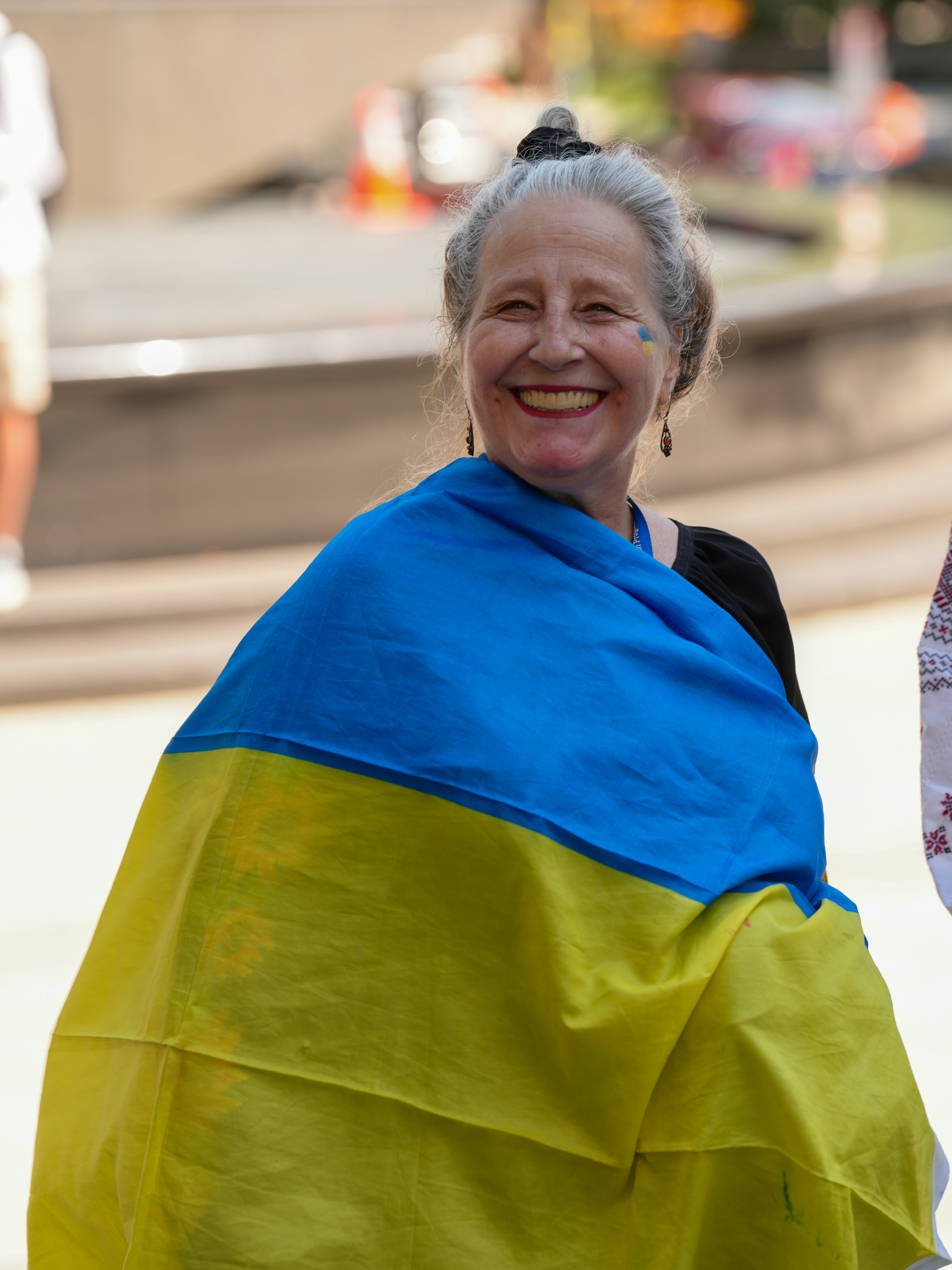 A smiling woman with grey hair draped in a blue and yellow flag