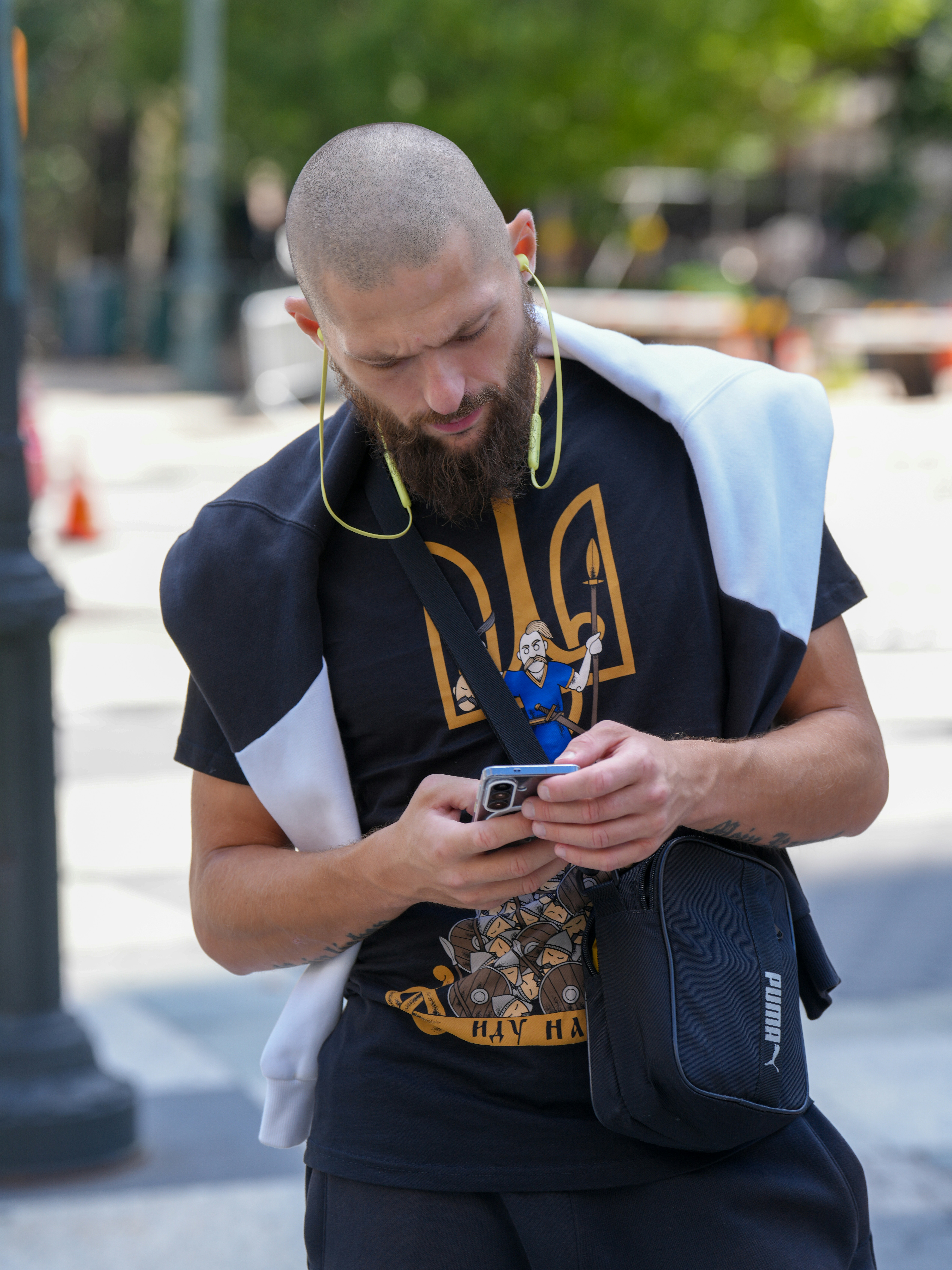 A man with a shaved head and beard looking at his smartphone outdoors