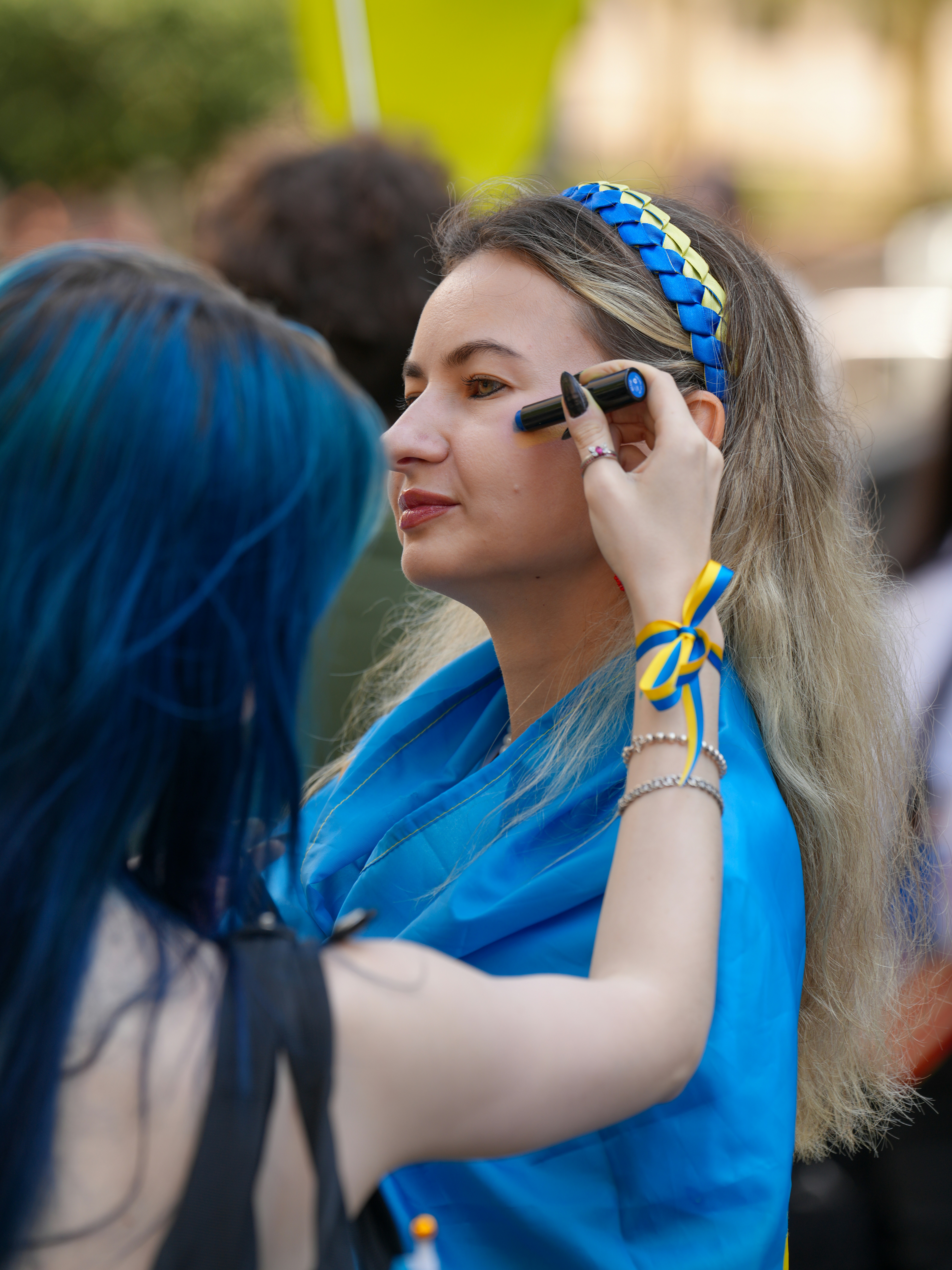 A person applying blue face paint to a woman wearing a blue and yellow headband