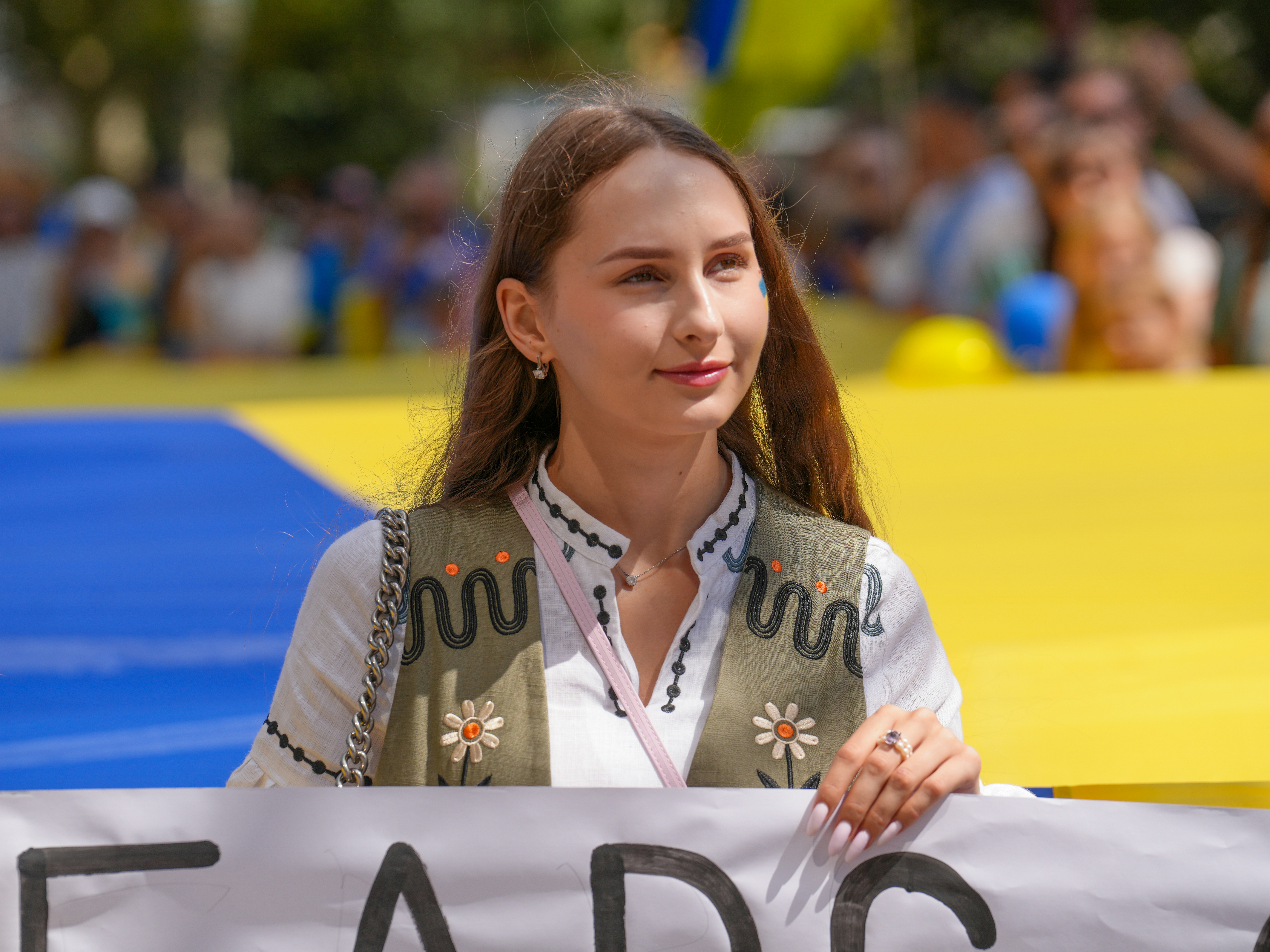 A woman in a white blouse and olive vest holding a sign outdoors
