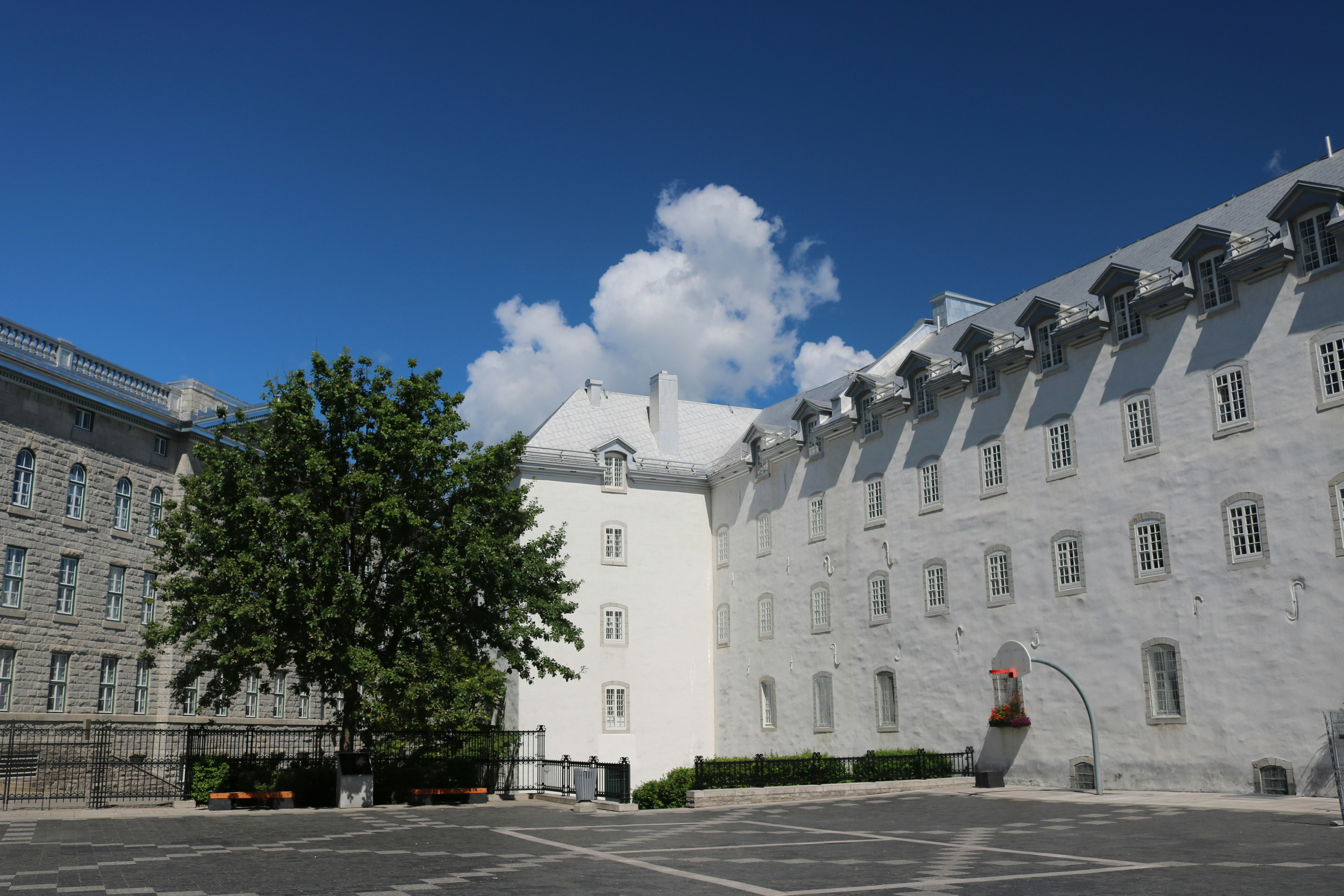 A large white building with many windows beside a stone structure and green tree