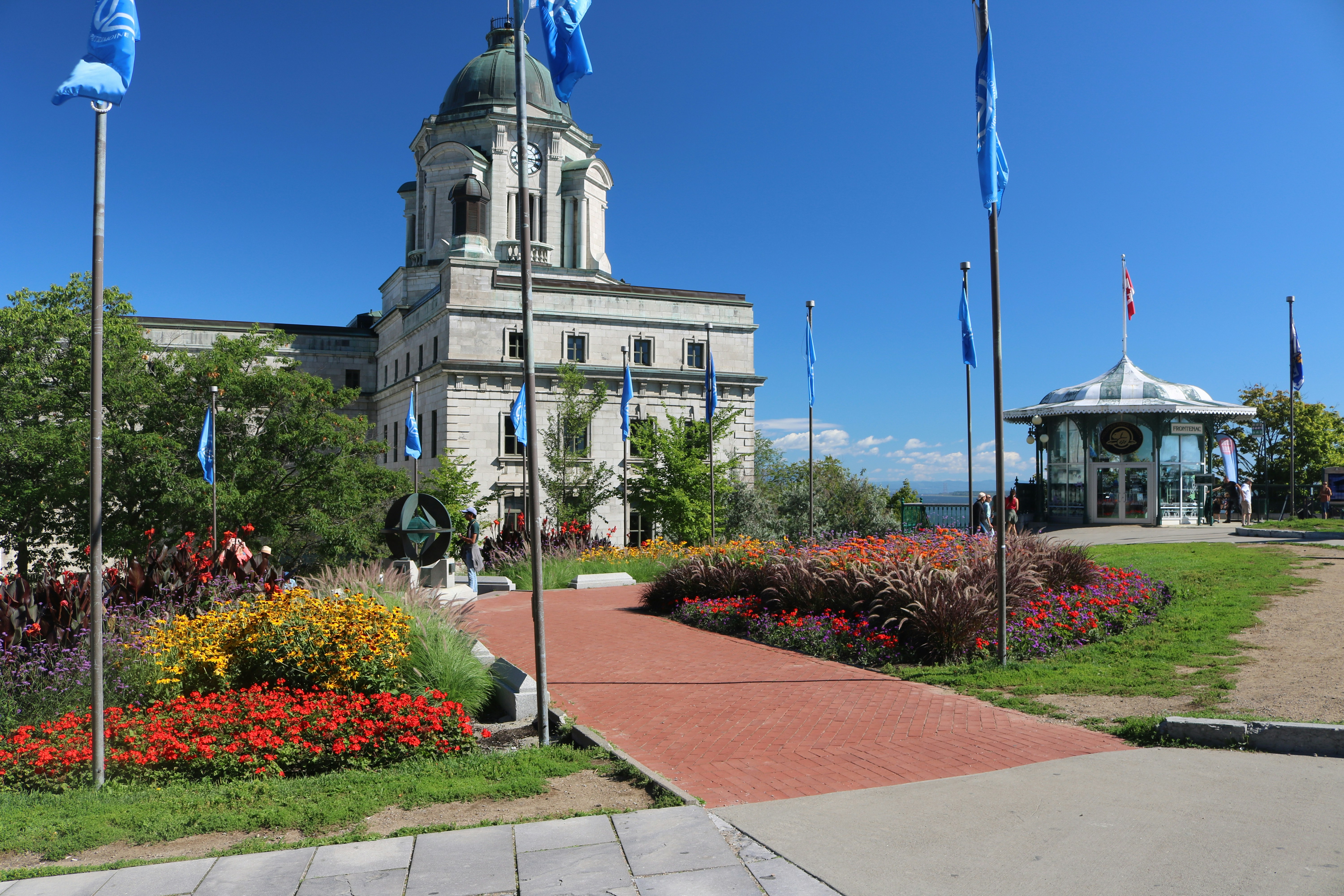 A stone building with a clock tower behind flower beds and a red path
