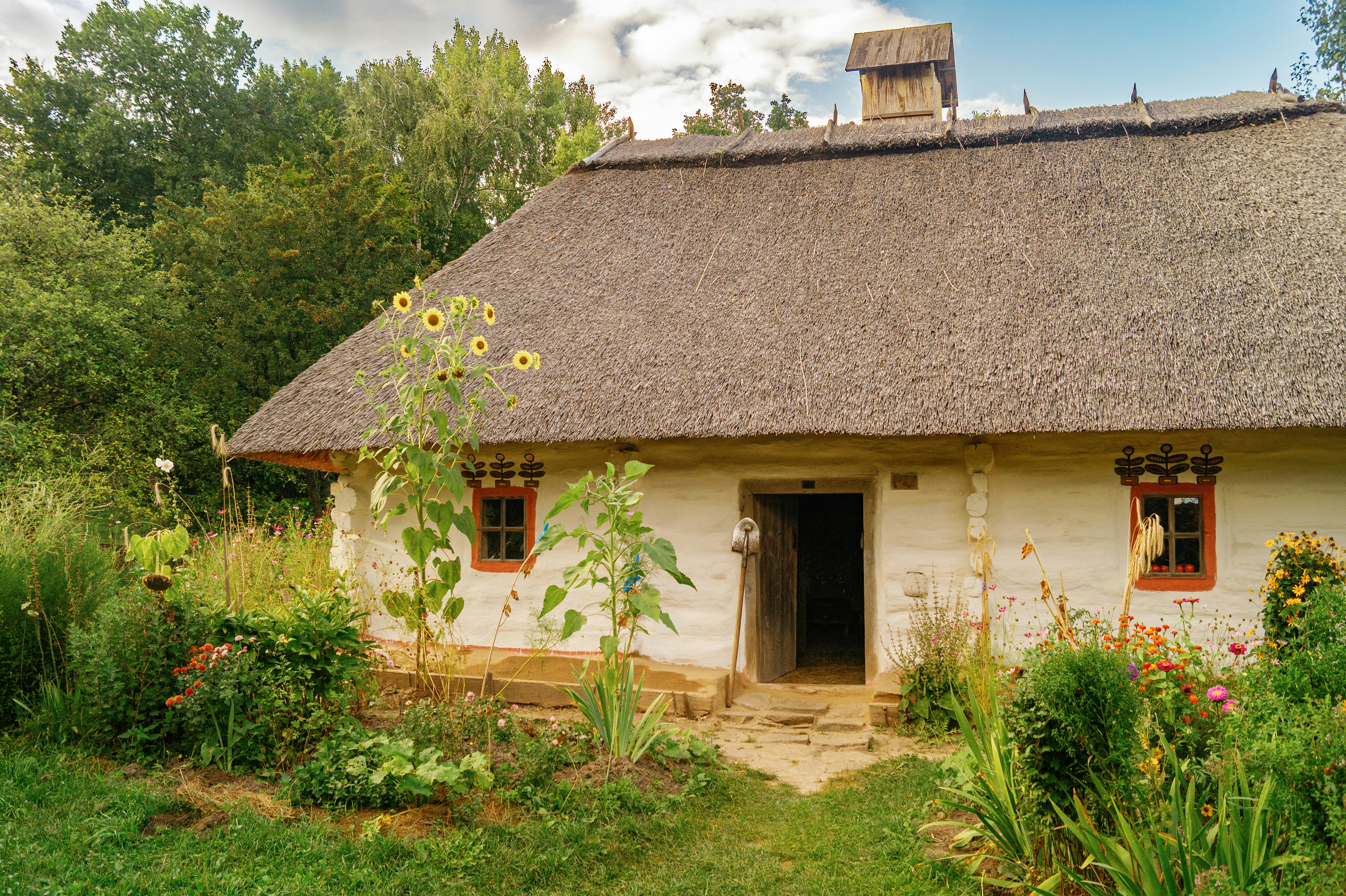 A traditional white cottage with a thatched roof surrounded by a vibrant flower garden